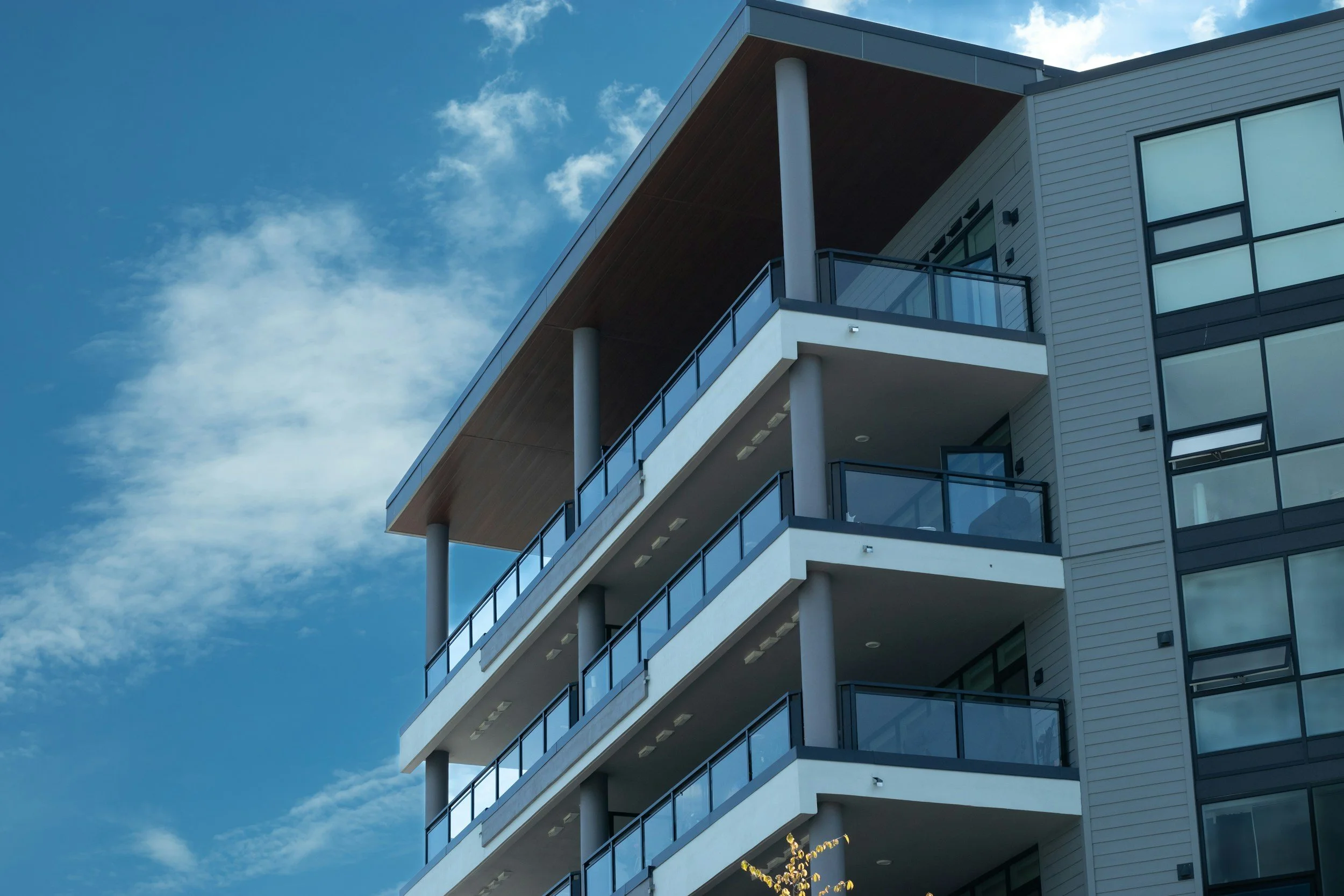 Modern multi-story apartment building with balconies and glass railings against a partly cloudy sky.