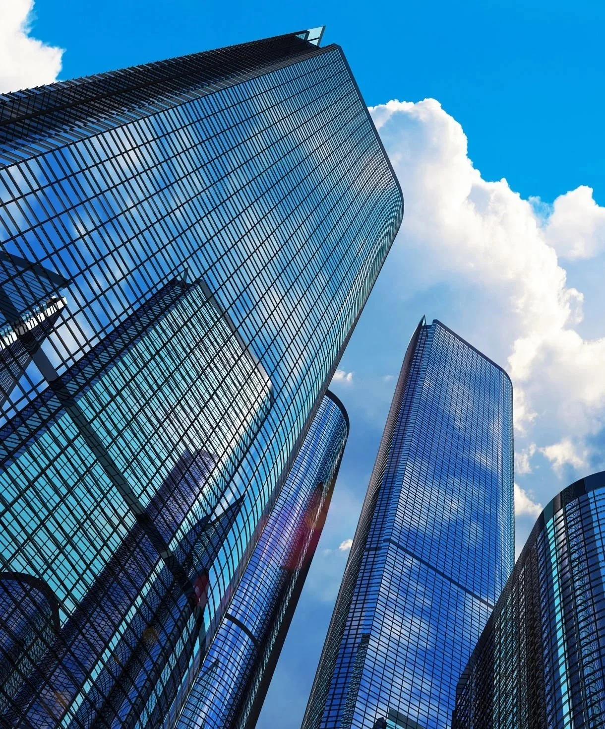 Low-angle view of tall glass skyscrapers reflecting the blue sky and white clouds.