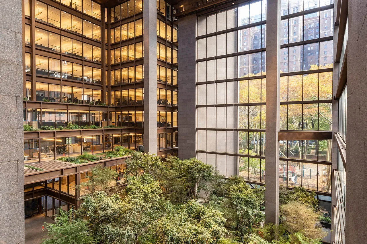 Interior view of a modern office building with large glass windows, multiple floors, and a central courtyard filled with trees and greenery.
