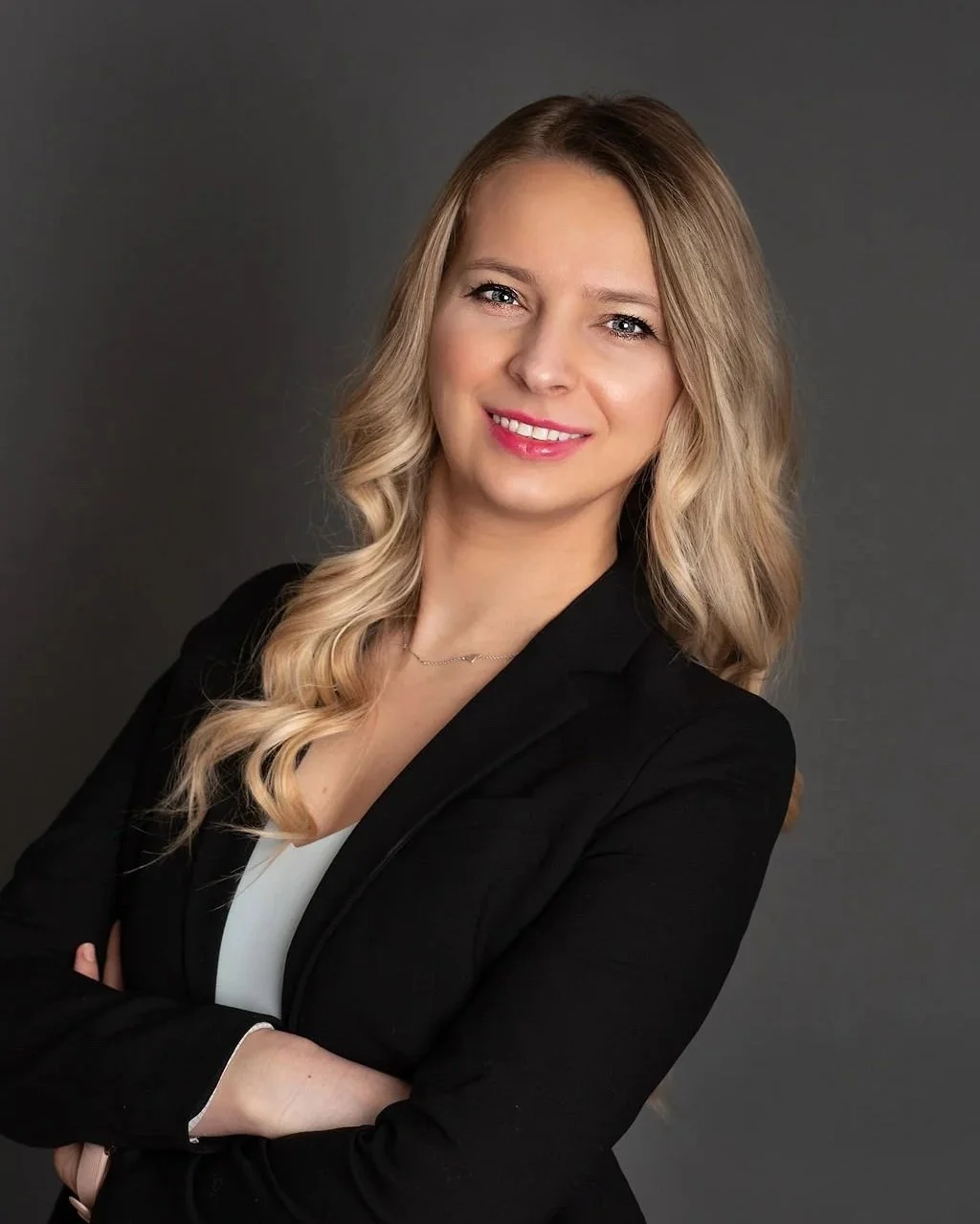 A portrait of Dr. Anna Urbaniak, founder of Mindfully Balanced NJ, smiling with arms crossed, against a dark gray background.
