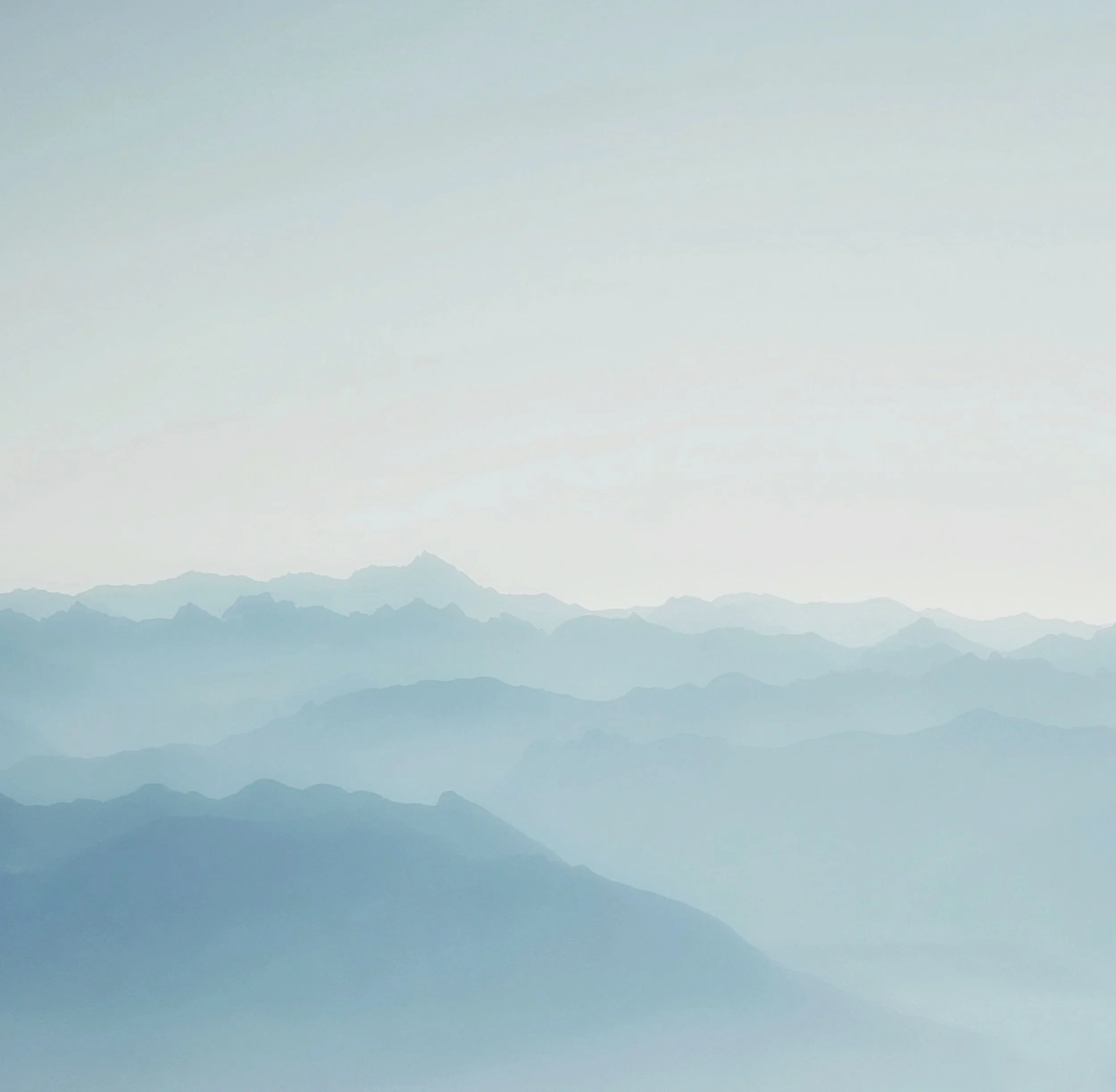 A panoramic view of distant mountain ranges with soft blue hues and a hazy sky.