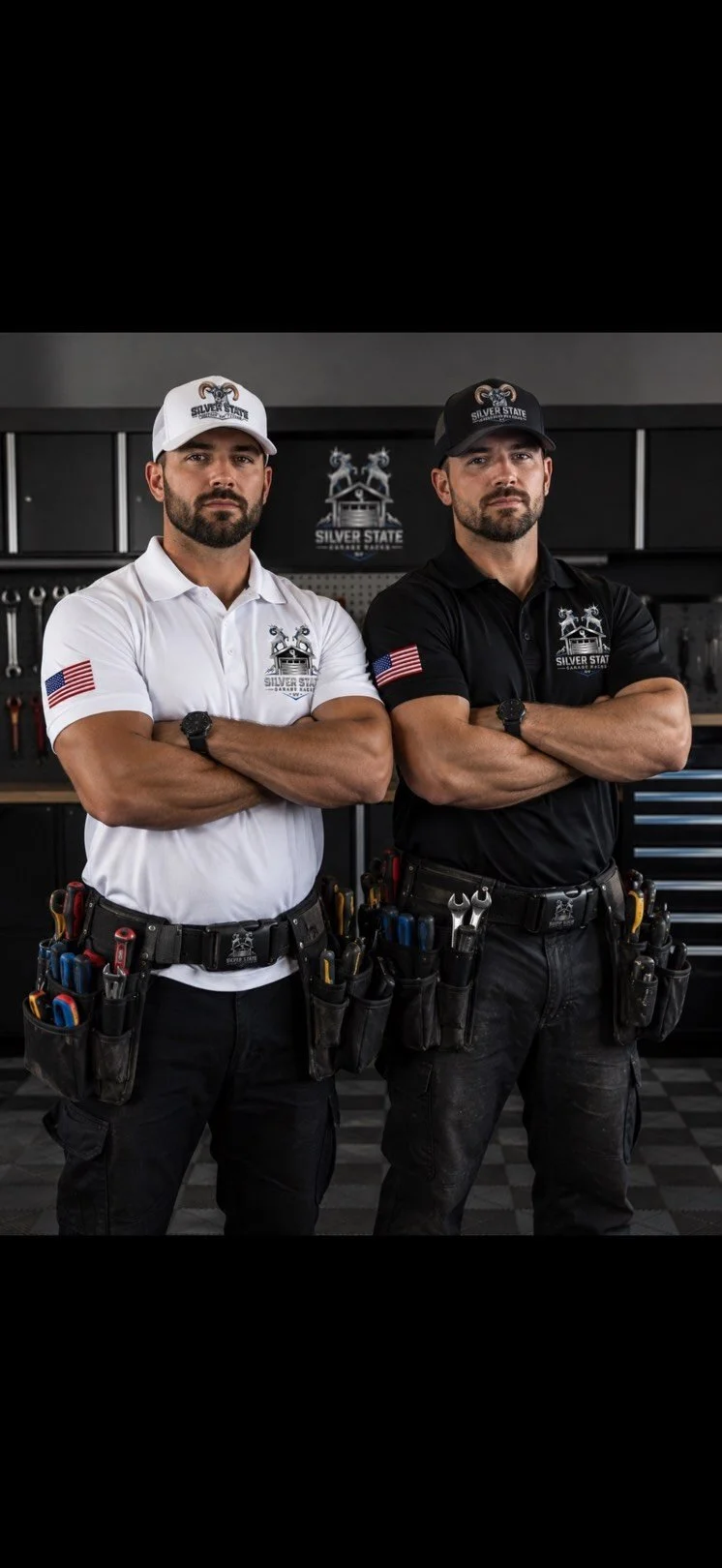 Two men in work uniforms with tool belts and crossed arms standing in a garage or workshop. One is wearing a white shirt and white cap, the other a black shirt and black cap, both with 'Silver State Garage' logos.