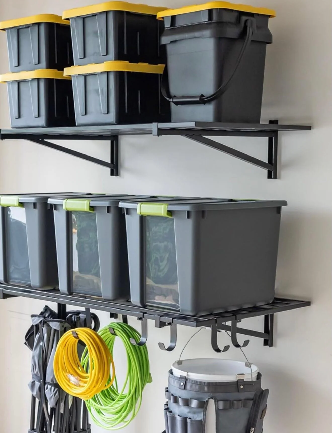 Garage wall shelf holding storage bins, with hanging garden hoses, tools, and a bucket.