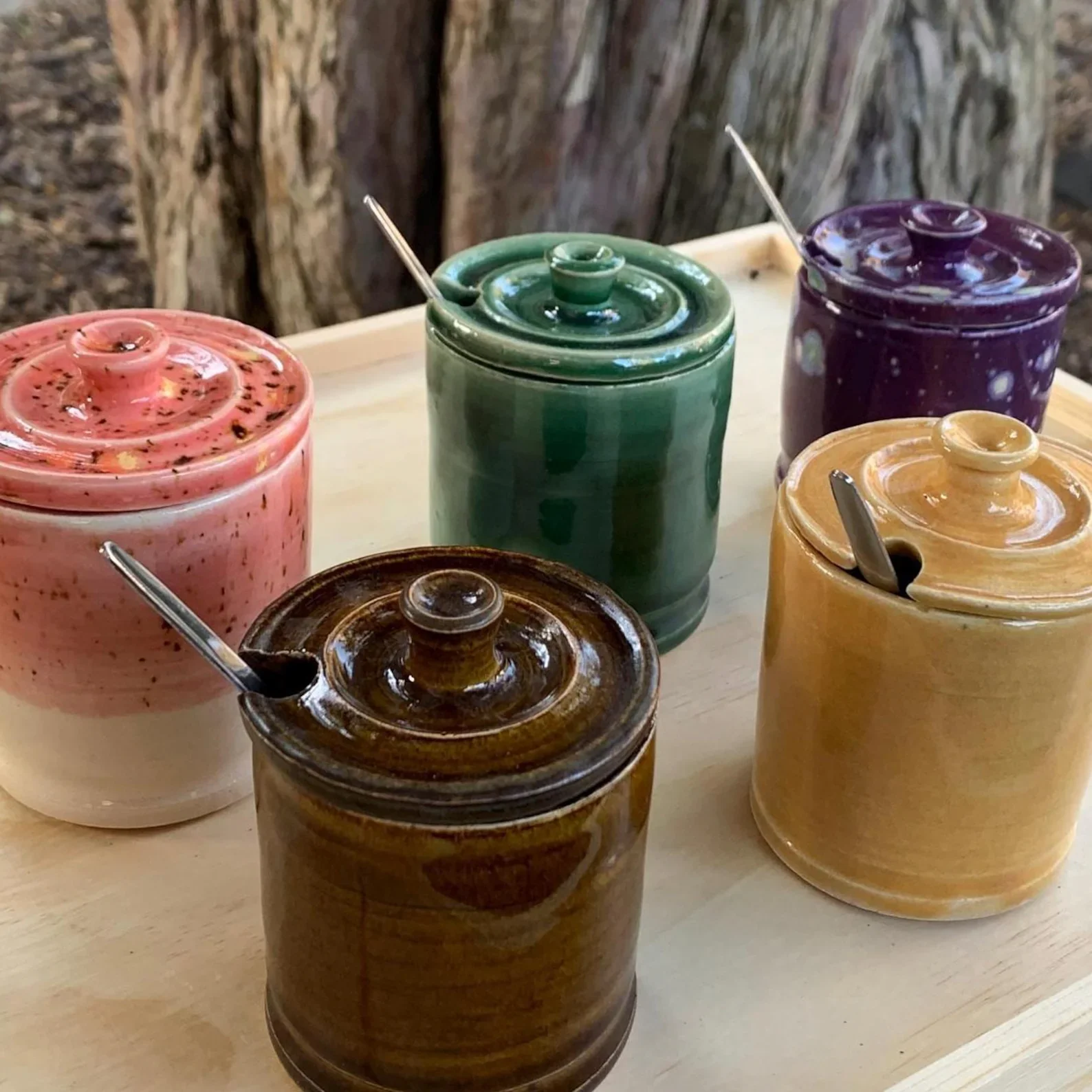 Colorful ceramic jars with lids and spoons on a wooden surface, set against a wooden background.