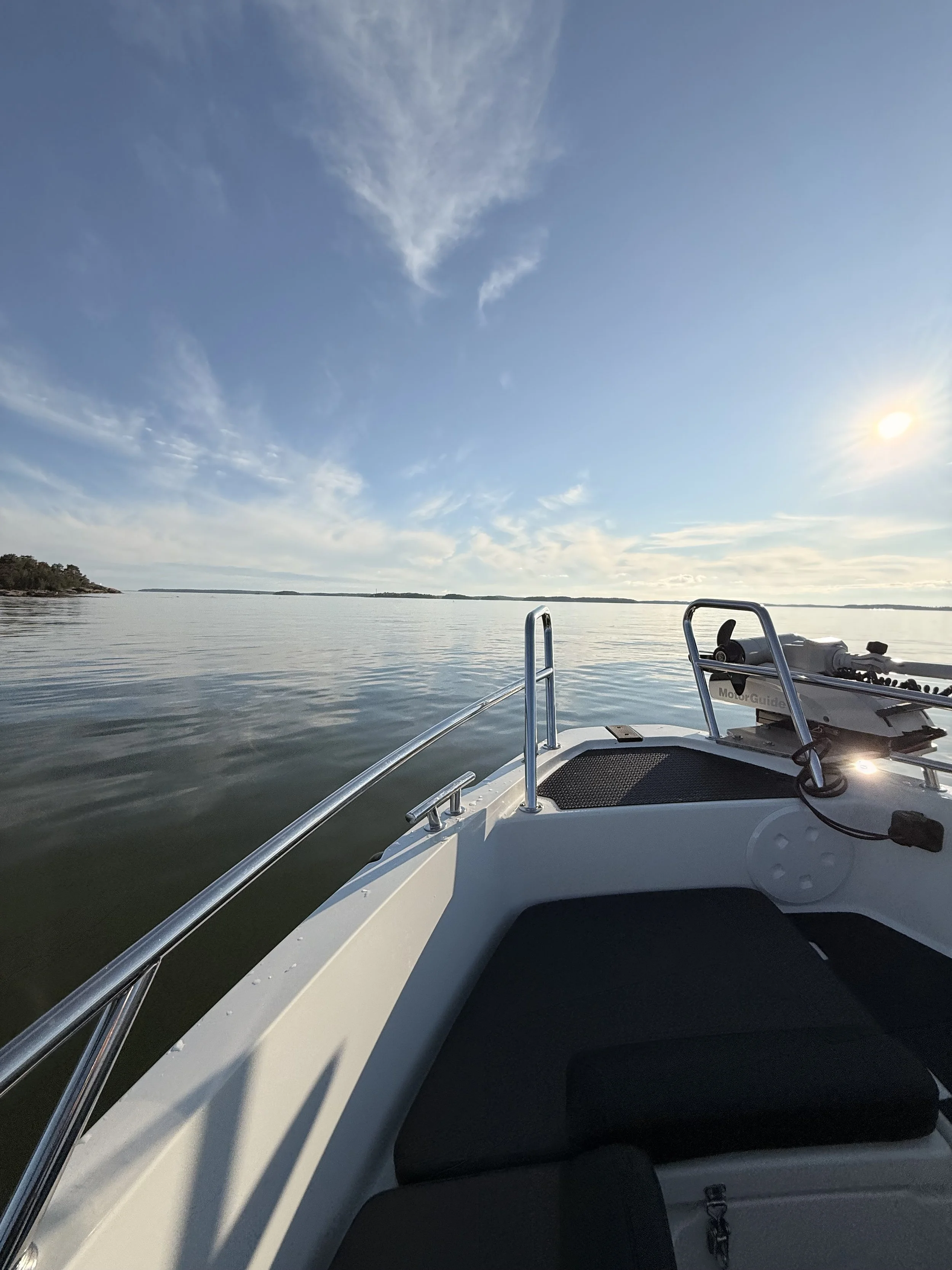 View from a boat on a calm lake with a clear sky, some clouds, and the sun low on the horizon. Part of the boat's bow and some equipment are visible in the foreground.