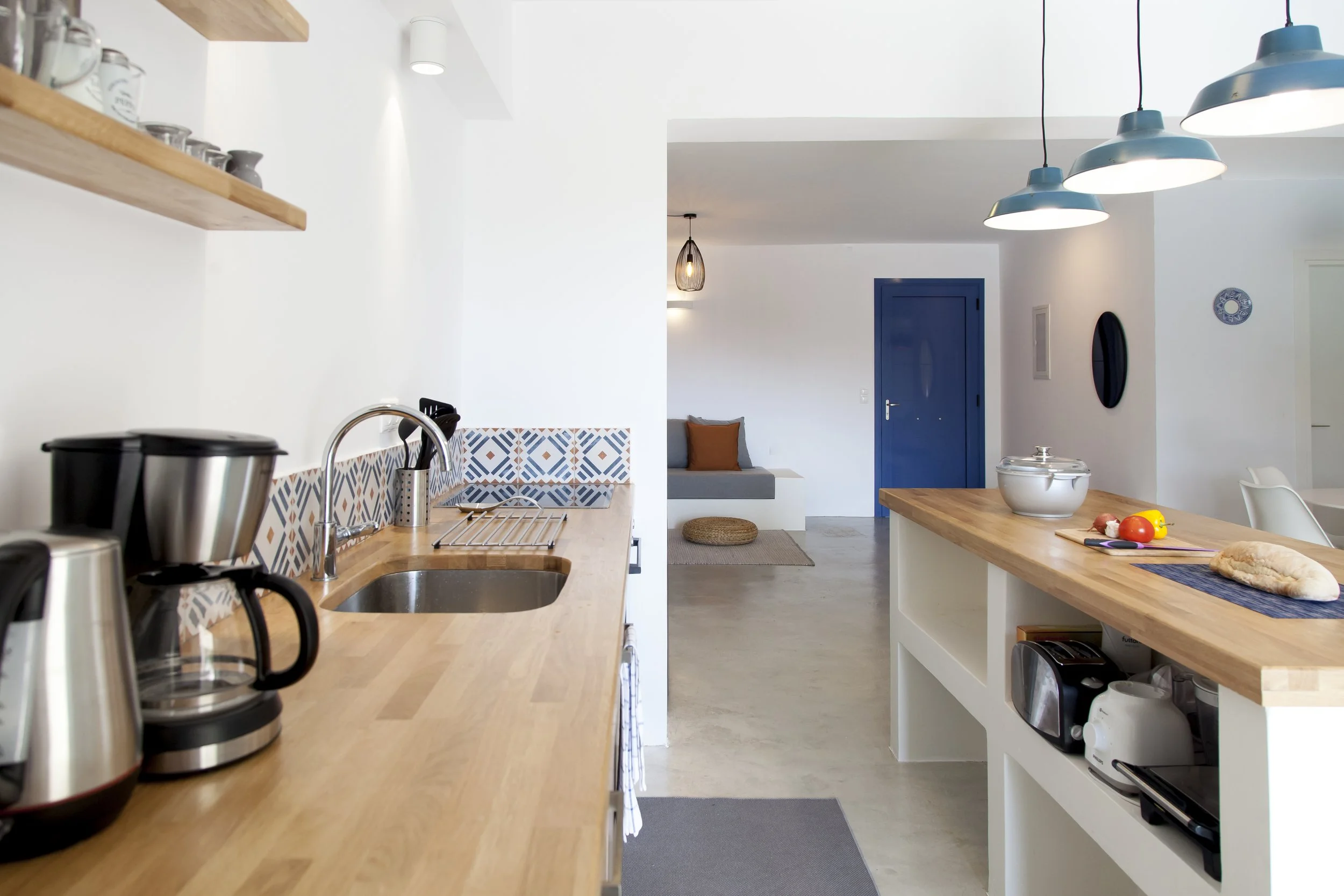 Modern kitchen with wooden countertops, blue door, hanging light fixtures, and various kitchen appliances and utensils.