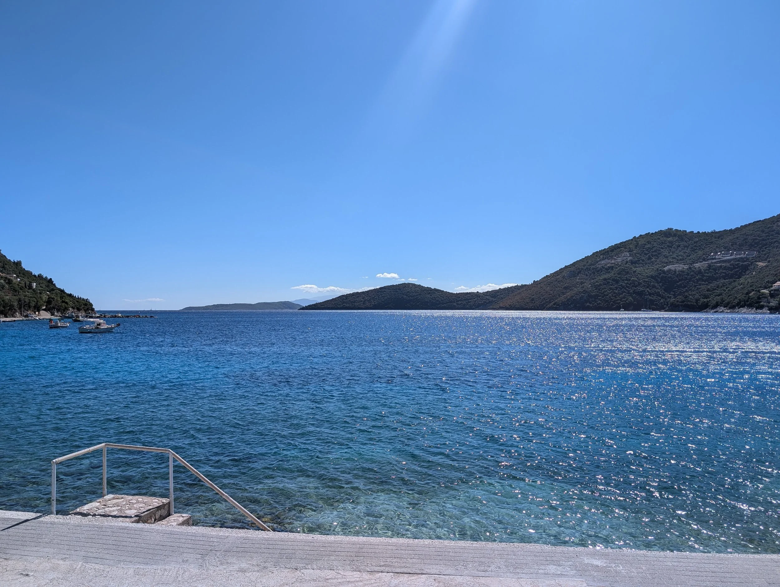 Scenic view of a large body of water with boats, green hills on either side, and a clear blue sky.