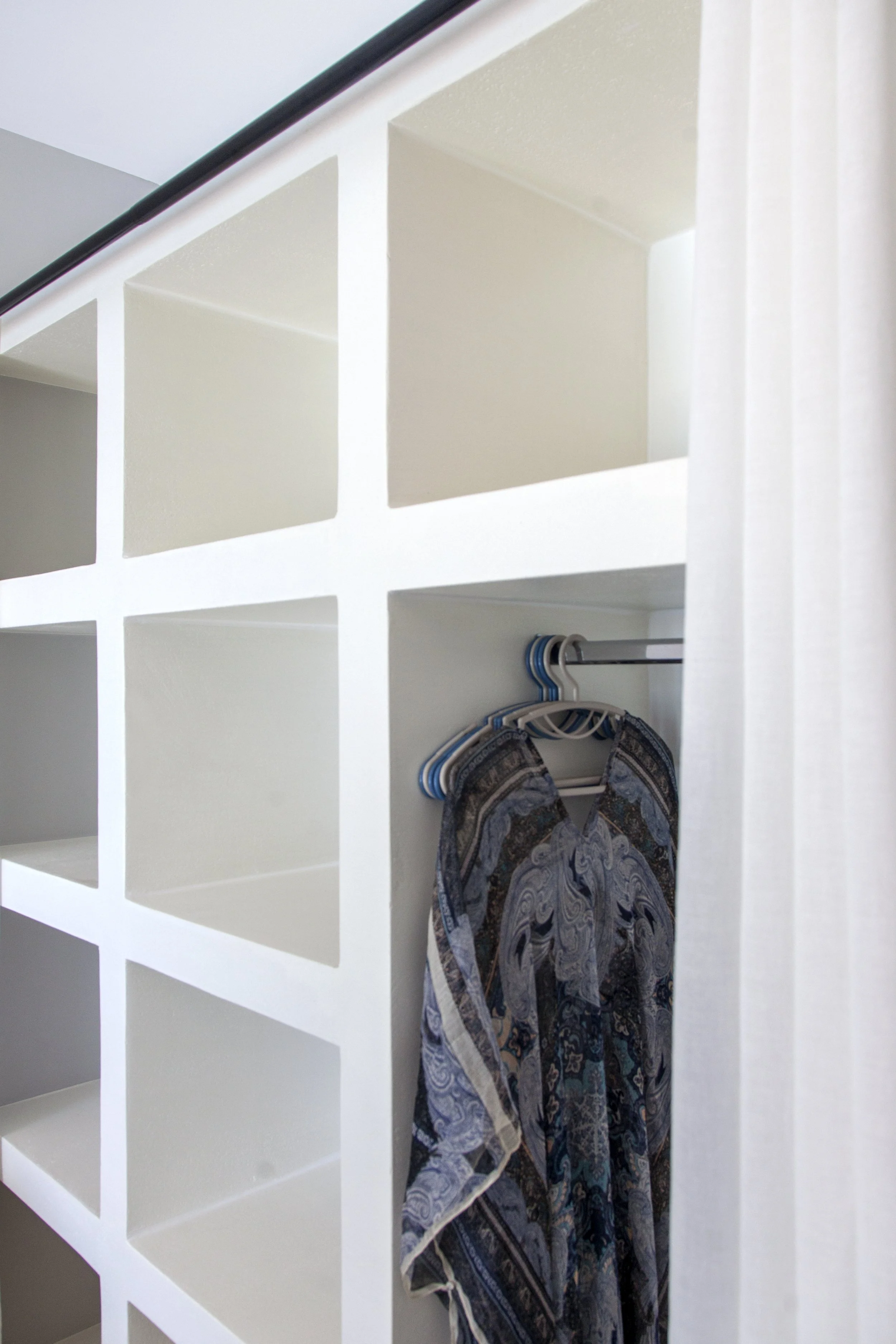 White cubed shelving unit with some clothing hanging on hangers.