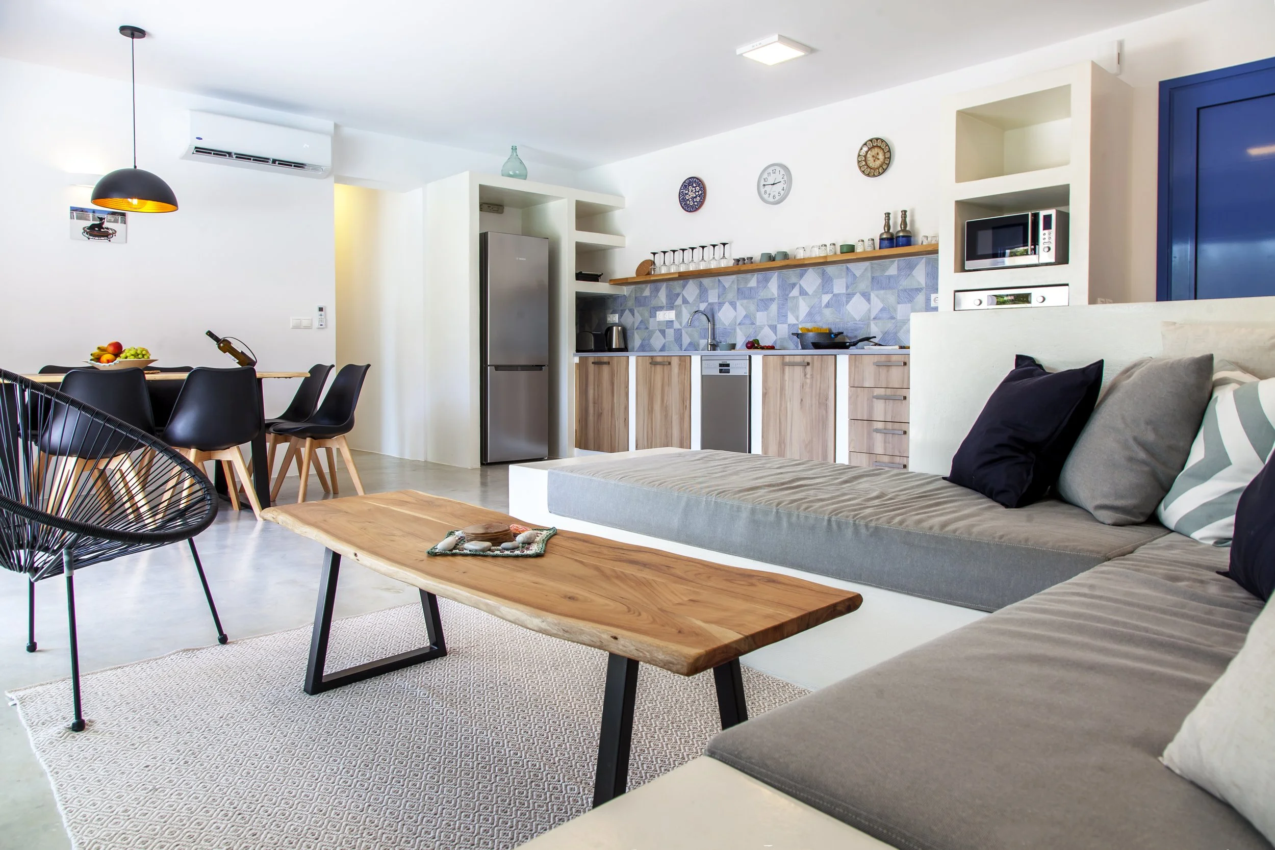 Open-concept living space with a kitchen, dining area, and sofa; modern decor with white walls, wooden accents, and geometric tile backsplash in the kitchen.