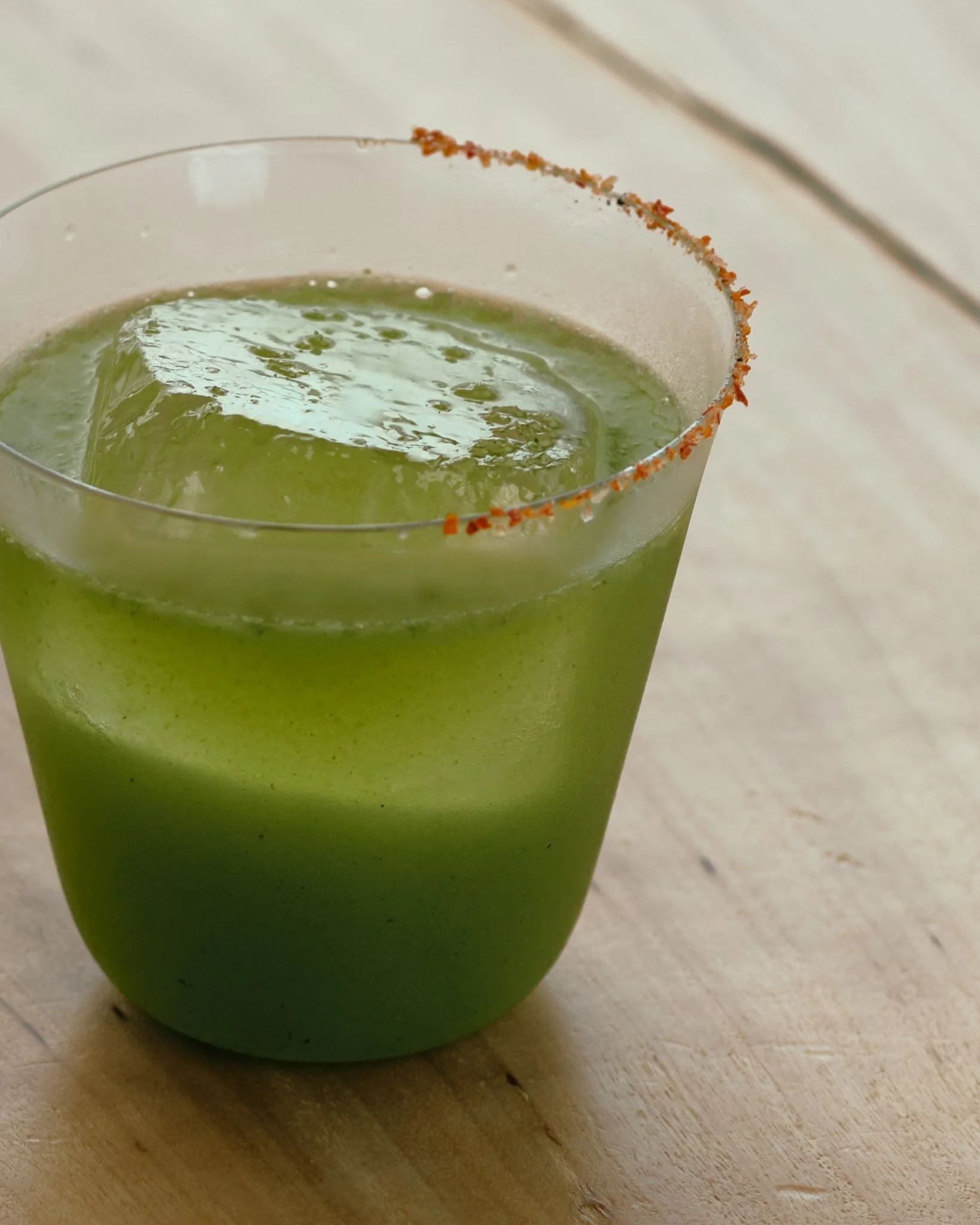 Close-up of a green cocktail in a clear glass with a salted rim on a wooden surface.