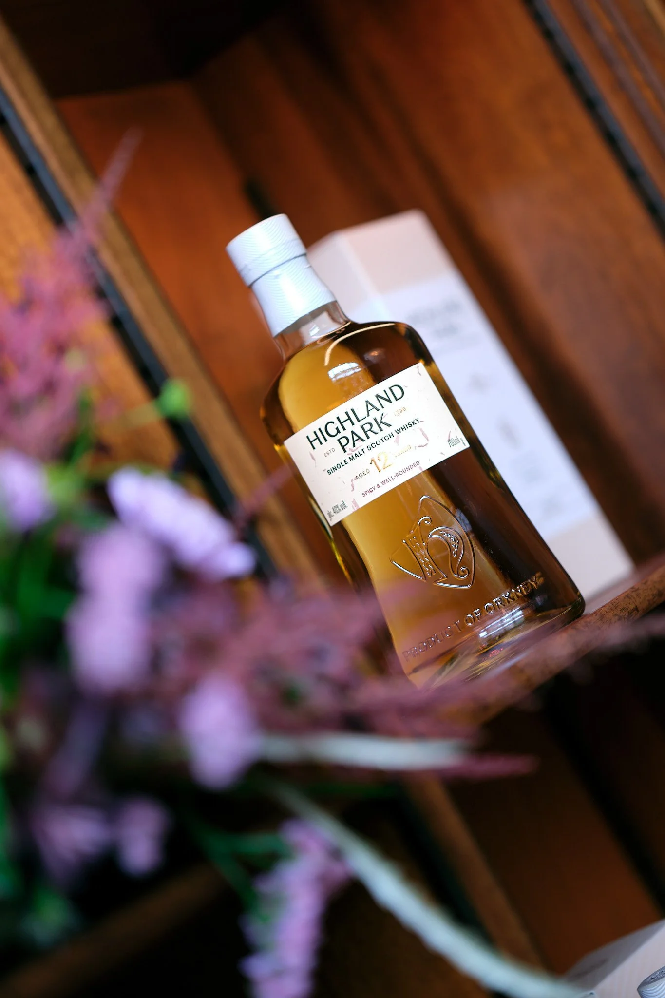 A bottle of Highland Park single malt Scotch whisky on a wooden surface with a blurred background and some flowers in the foreground.