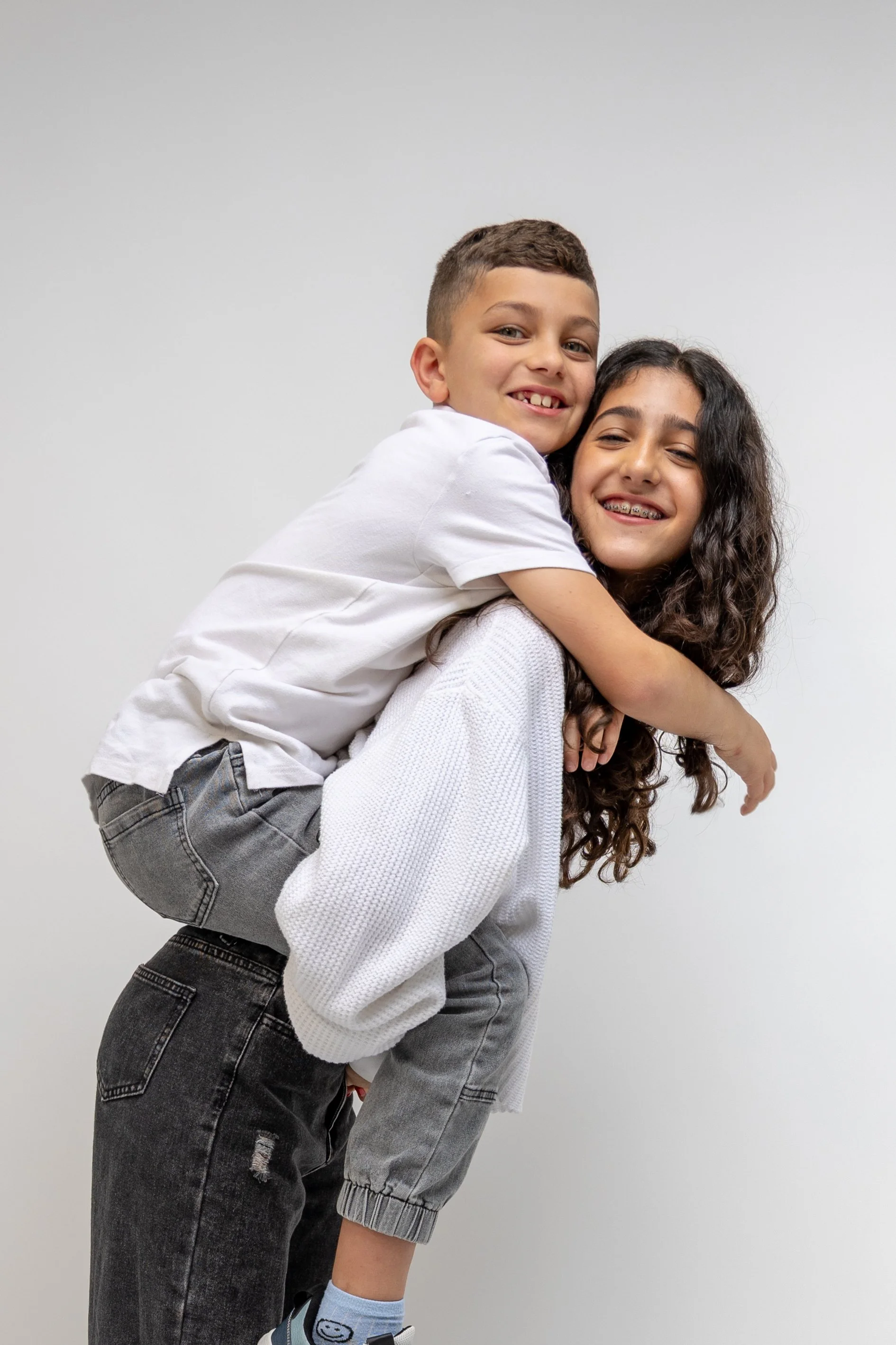 A woman giving a piggyback ride to a smiling young boy with missing front teeth, both wearing casual clothes, on a plain background.
