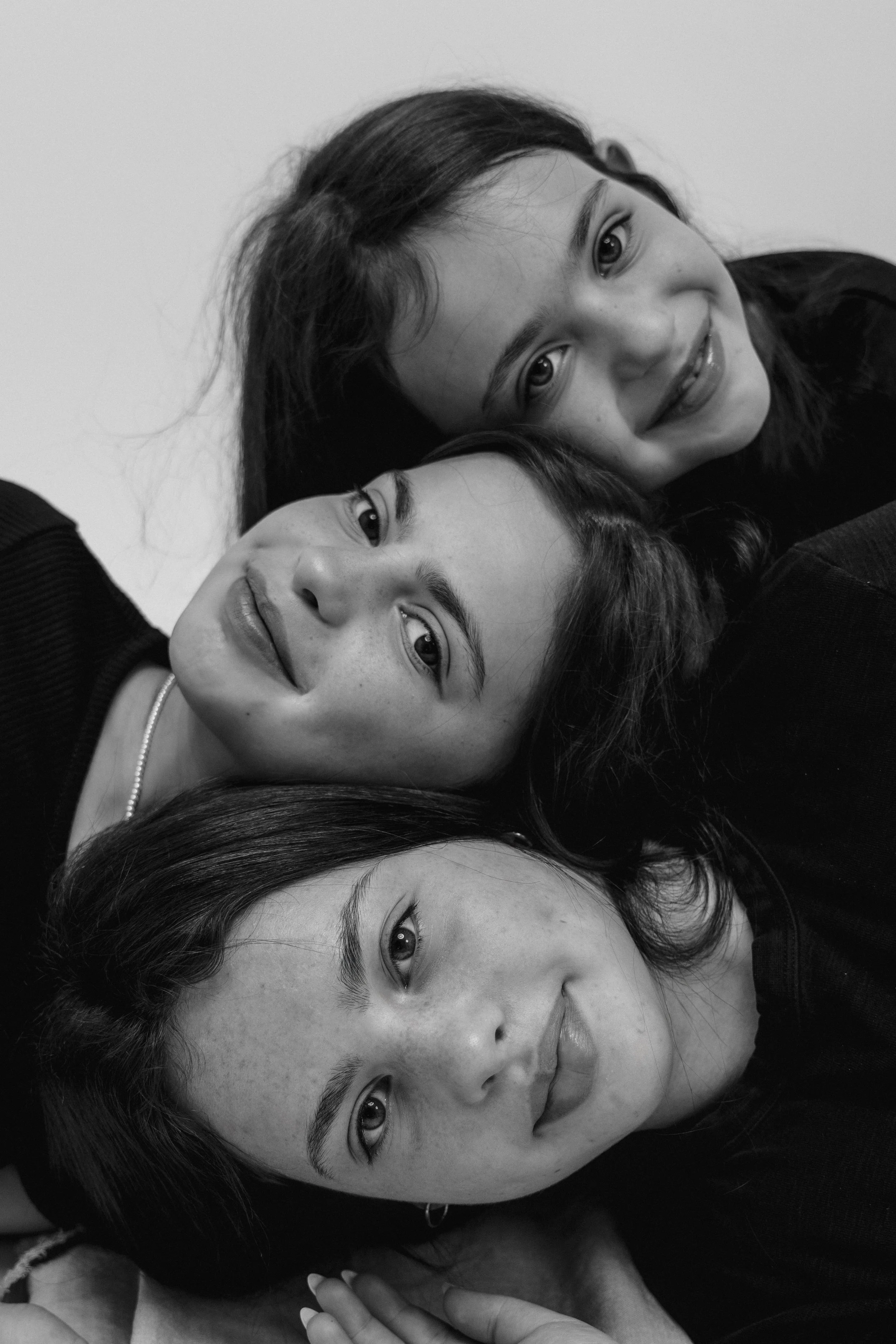 Close-up of four young women lying down with their heads stacked, looking at the camera, smiling and making eye contact.