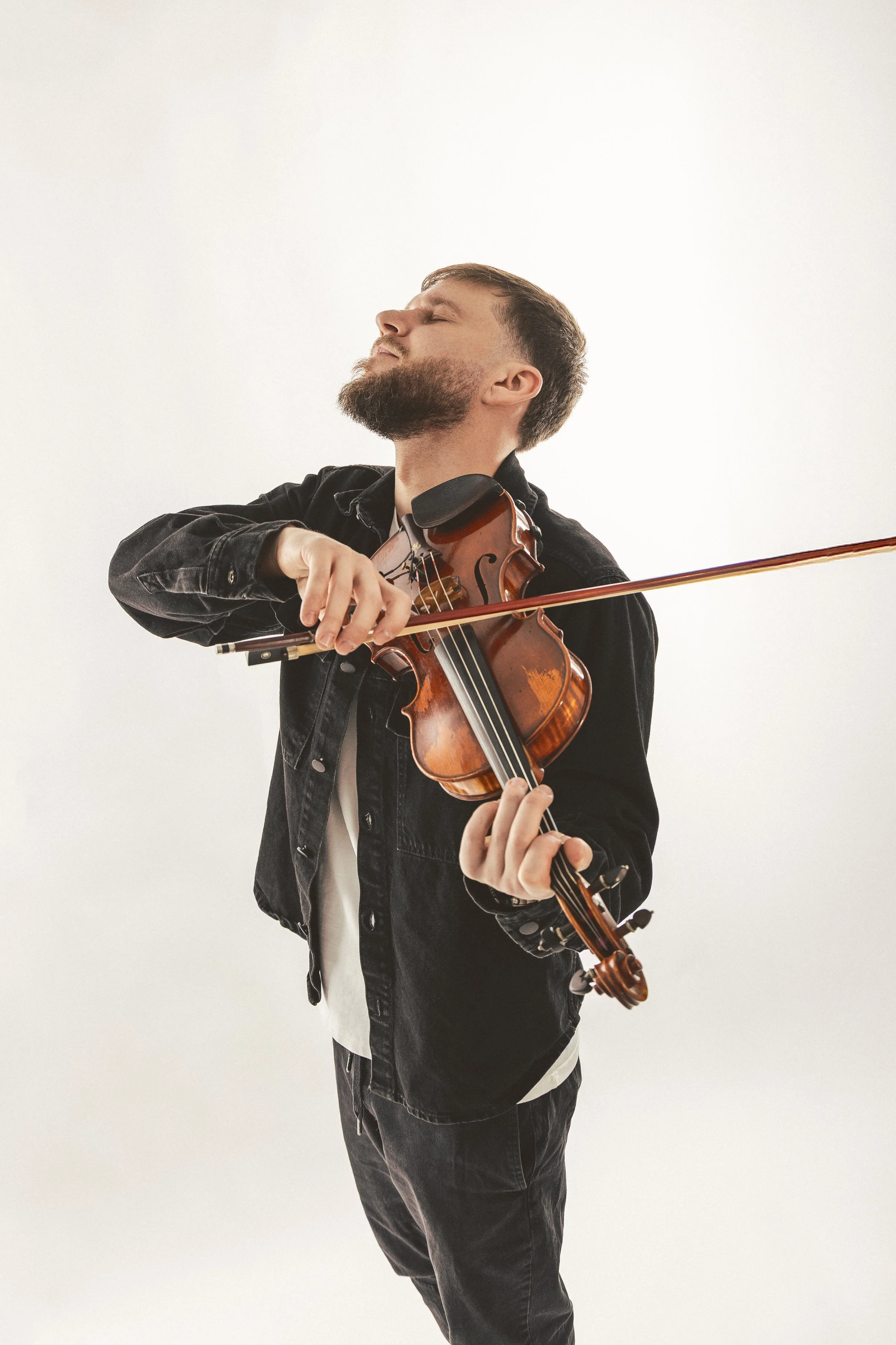 A man with a beard and black hair playing a violin against a plain white background.