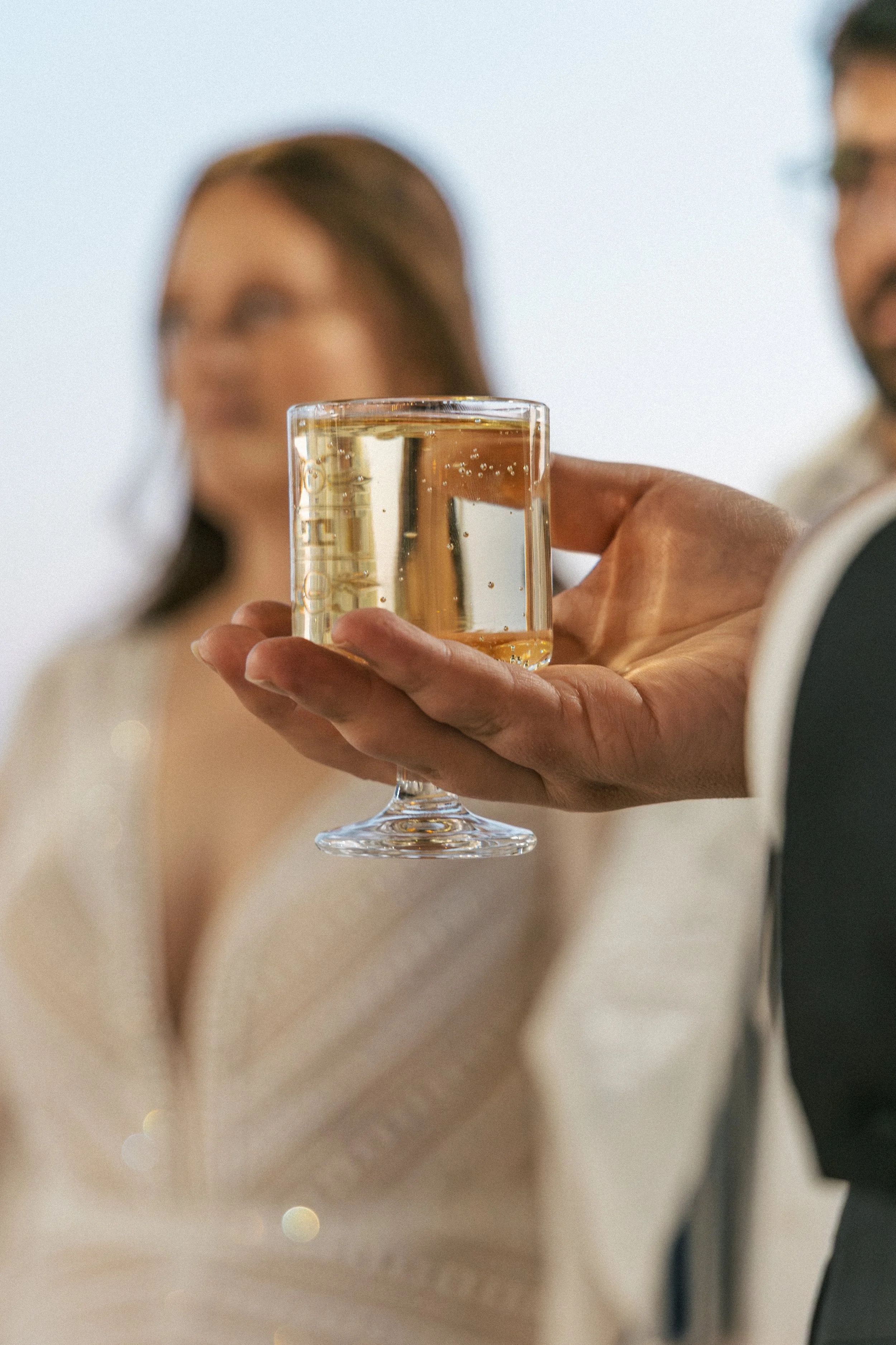 A person in a white outfit holding a glass of champagne at a celebration or gathering.