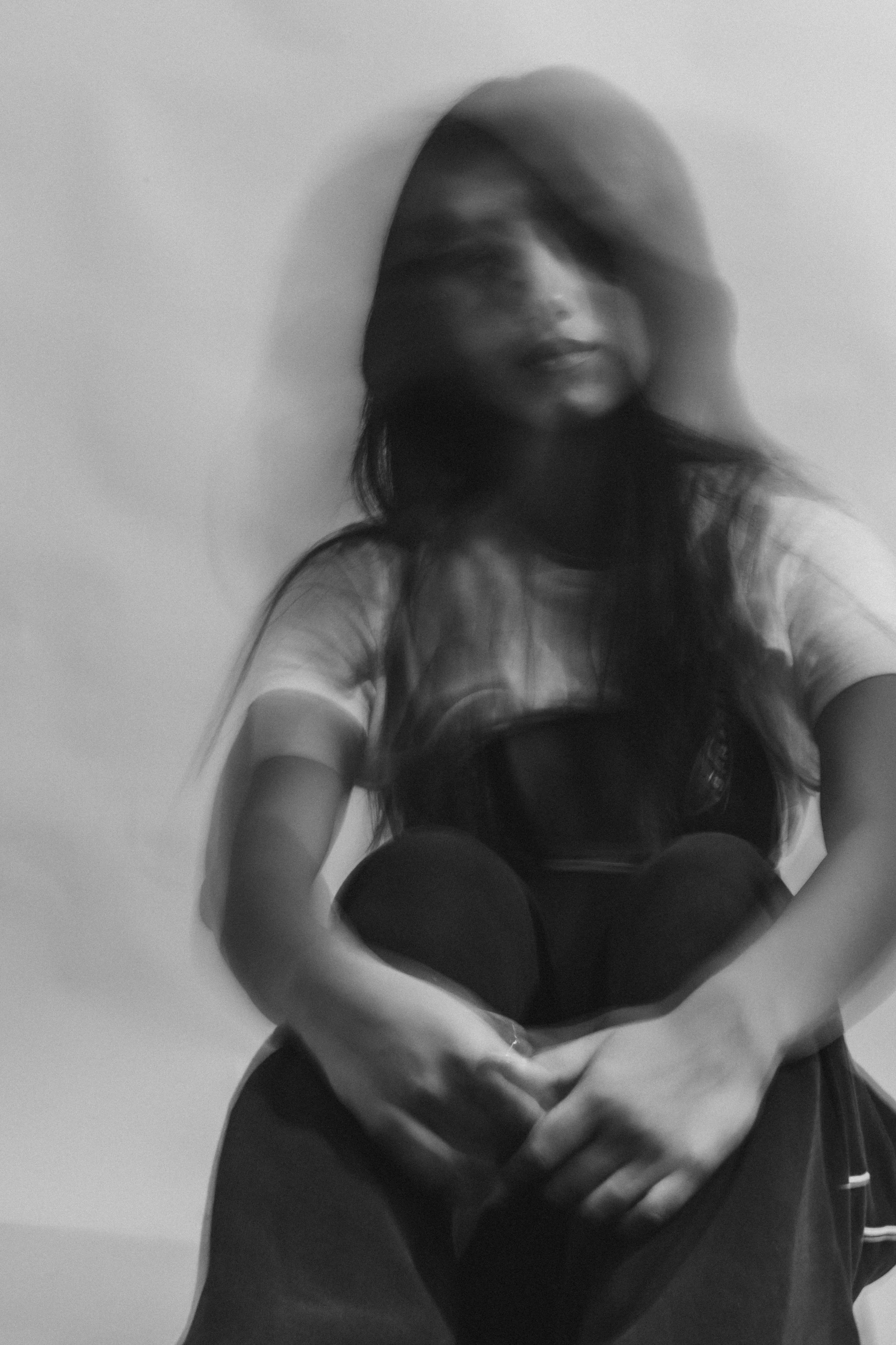 Black and white photo of a woman with long hair, wearing a hat, sitting with her arms crossed, and looking at the camera.