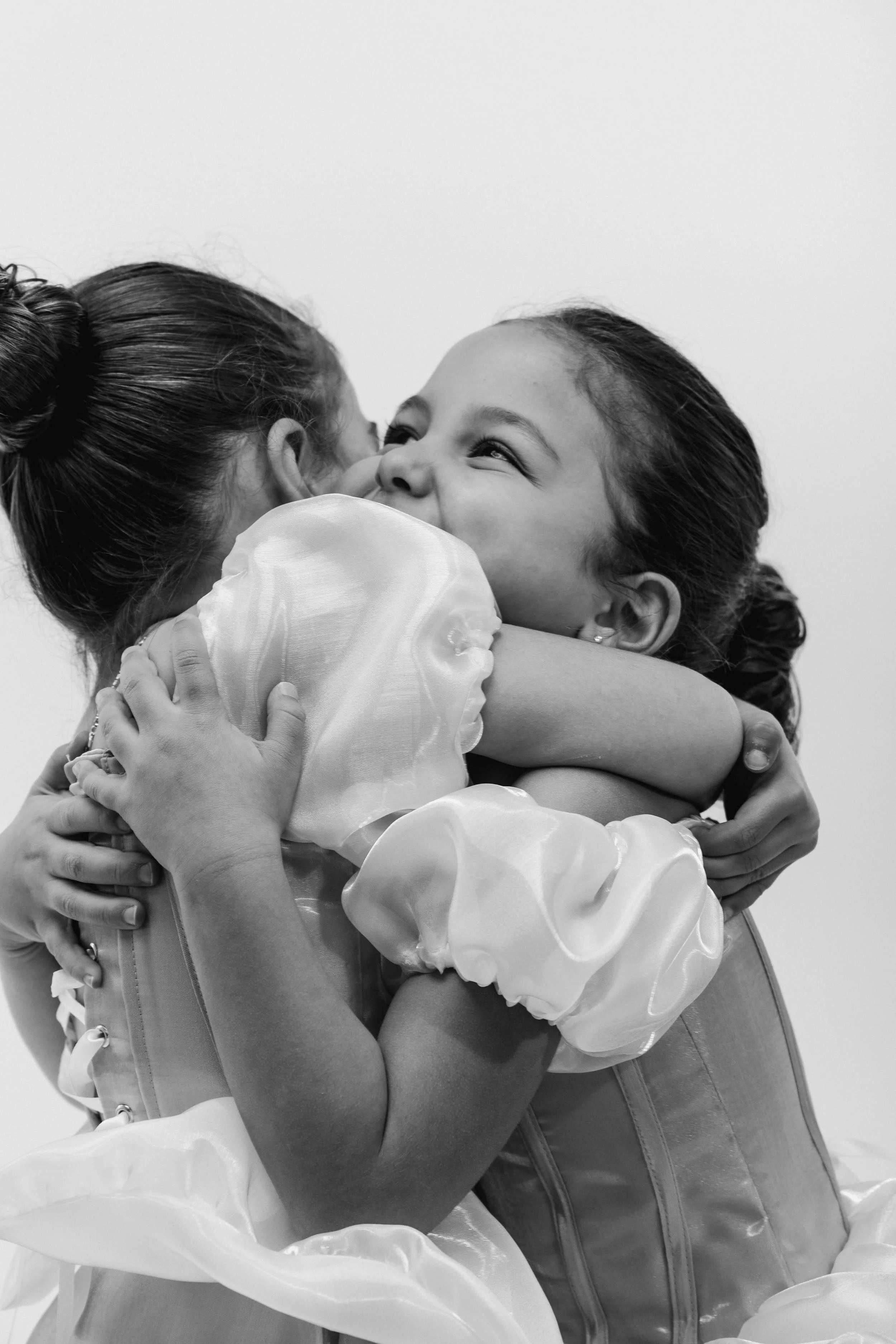 Two women hugging and smiling, wearing formal dresses, in a black and white photo.