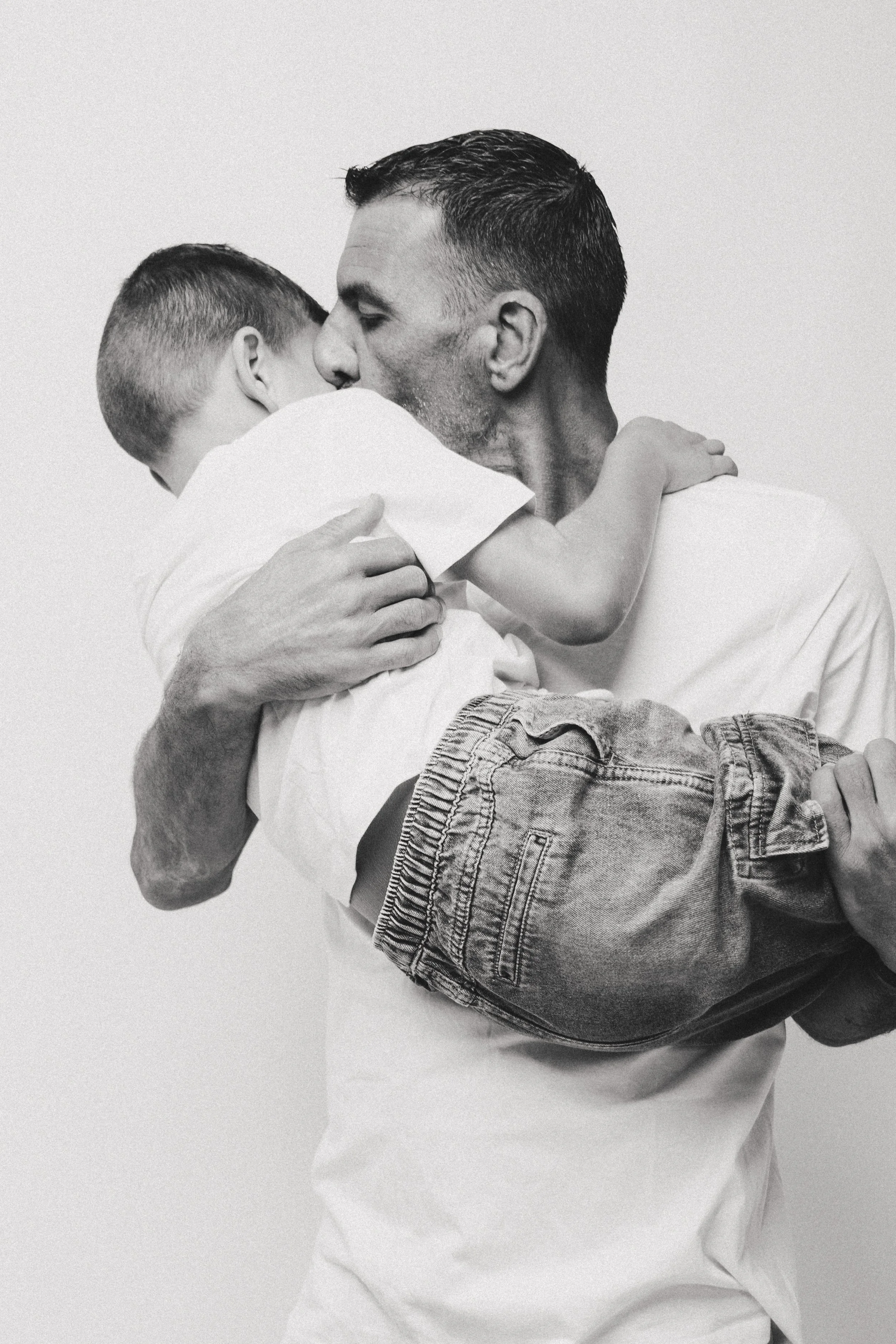 A man holding a child close to his face, both with eyes closed, in a tender embrace on a plain background.