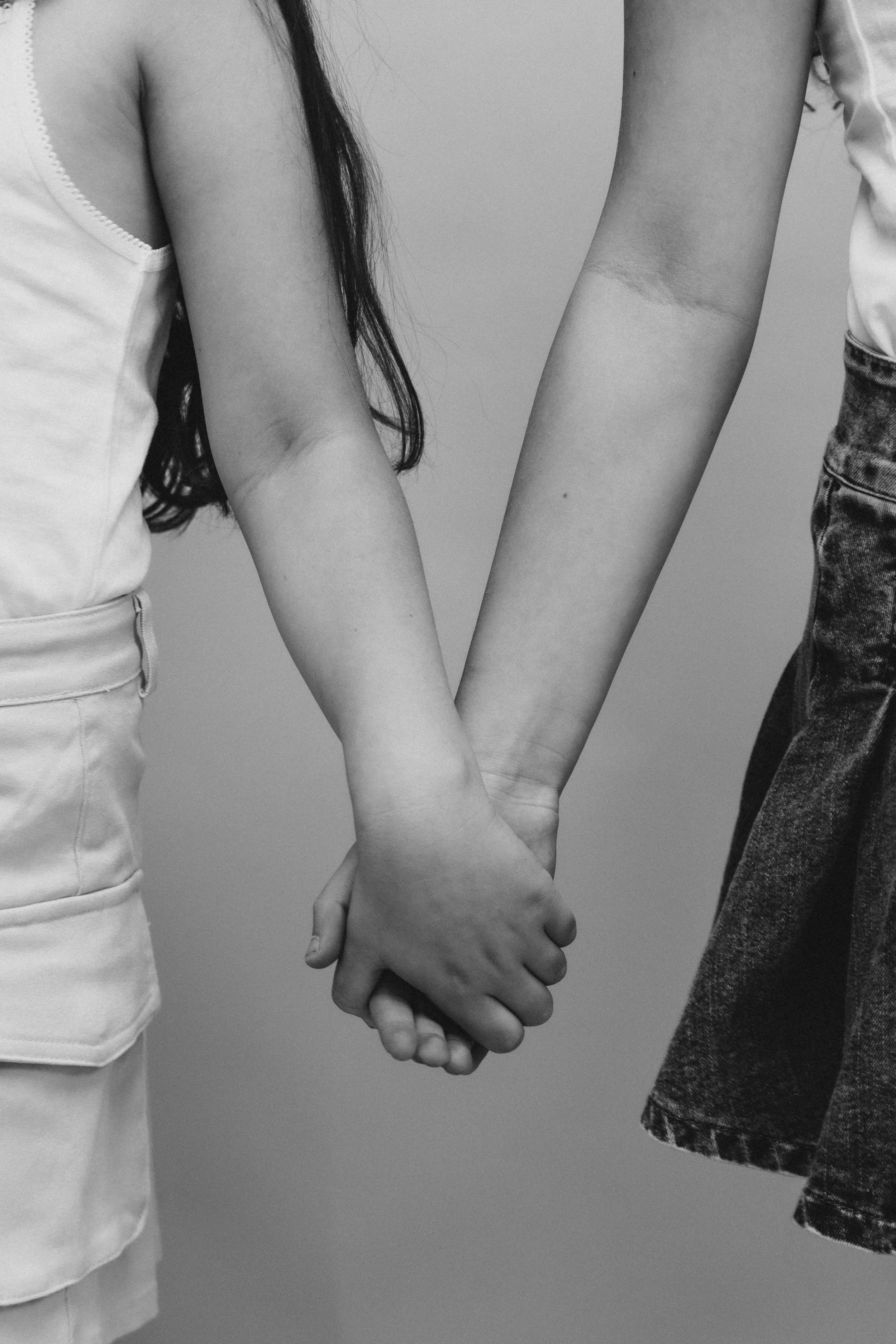 Two people holding hands, one wearing a white sleeveless top and the other wearing a dark patterned pants.