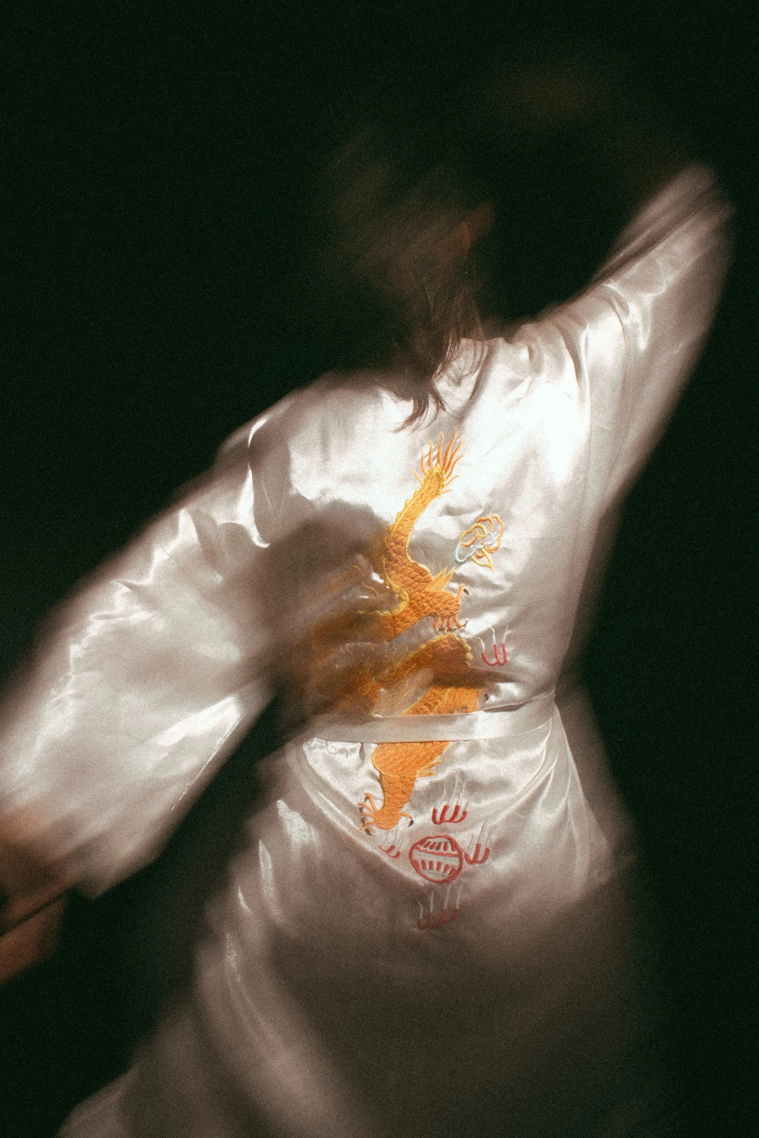 Close-up of a satin jacket with embroidered golden dragon and red Chinese characters, on a dark background.