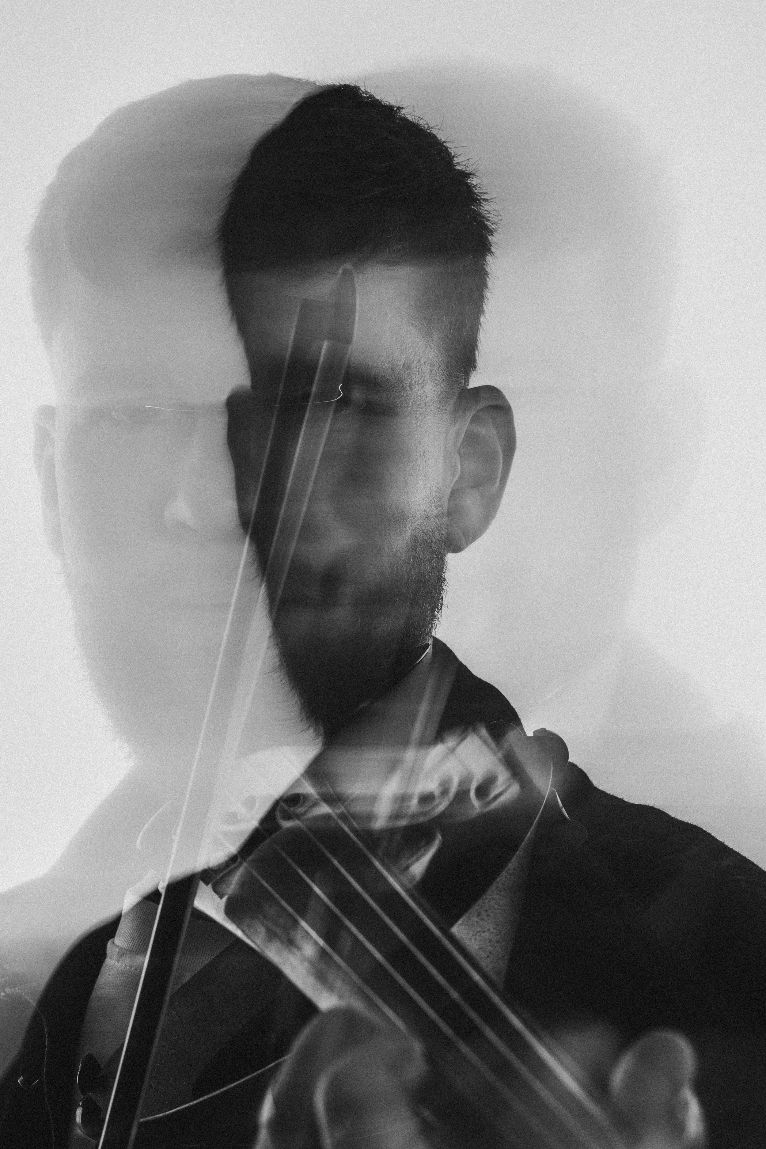 A black and white photo of a man with short hair and a beard seen through a glass or mirror, with reflections and slight distortions obstructing the view.