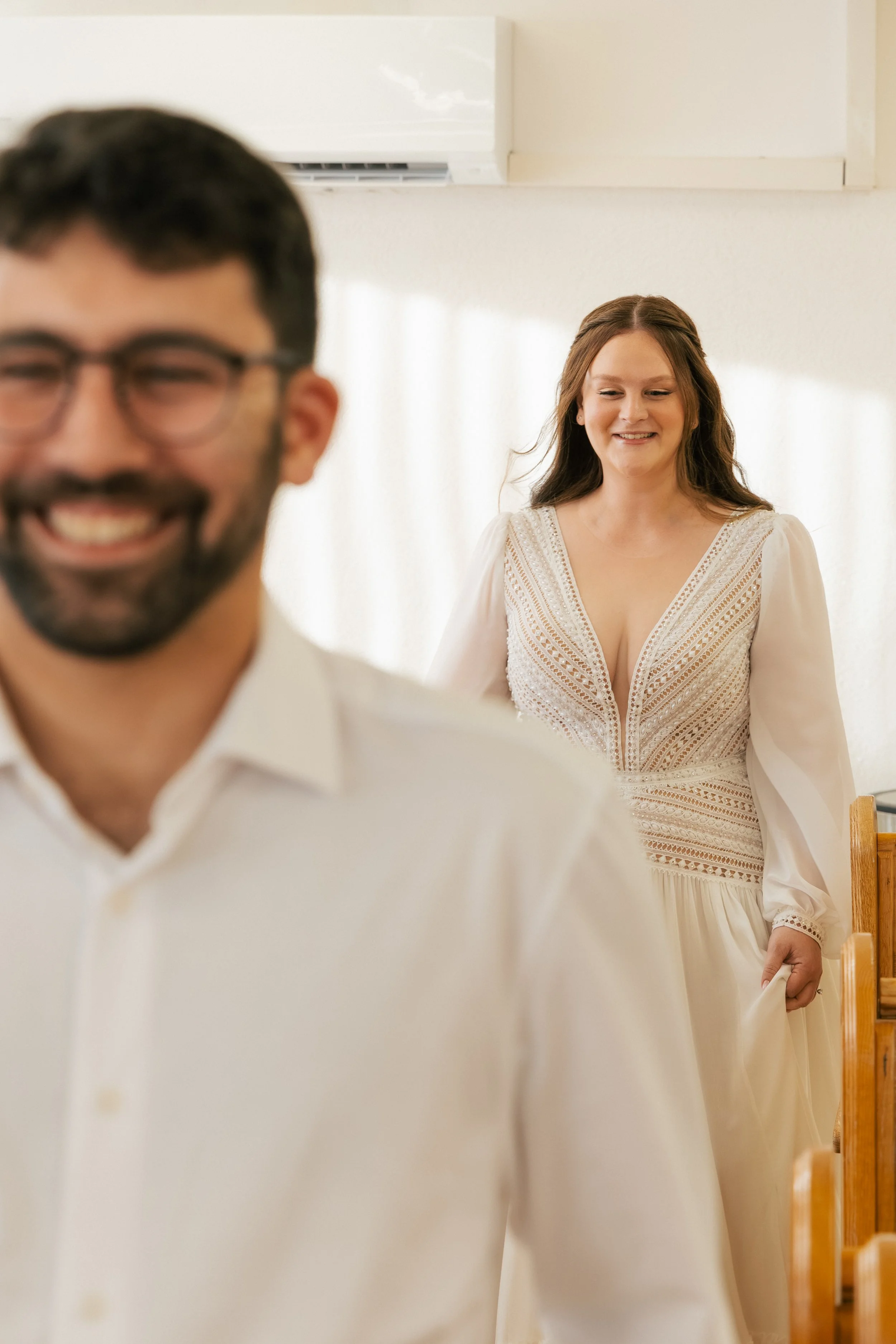 A smiling woman in a white dress watching a man in glasses who is also smiling.