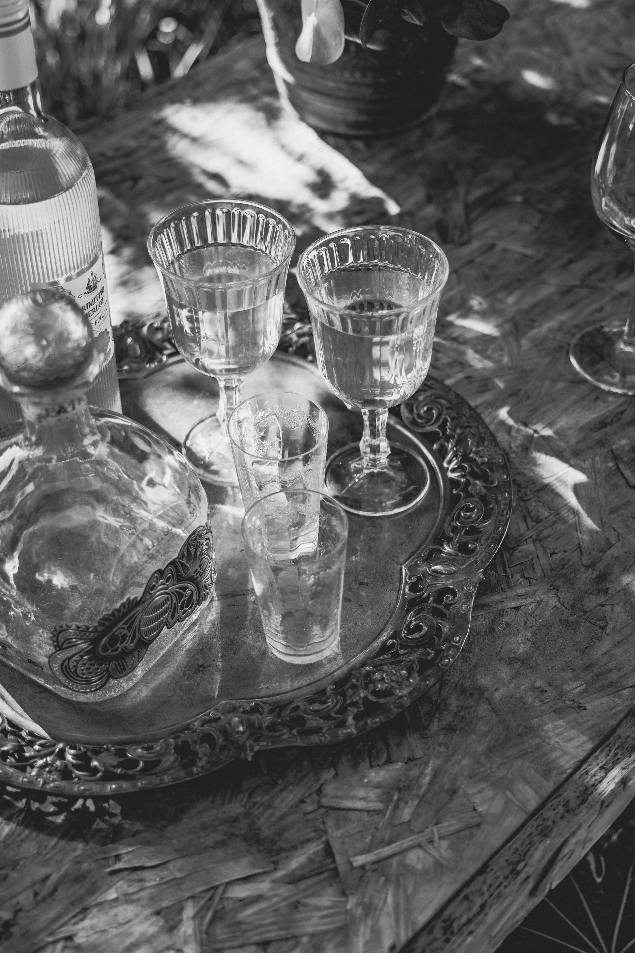 Glassware and bottle on a decorative tray placed on a wooden table outside.