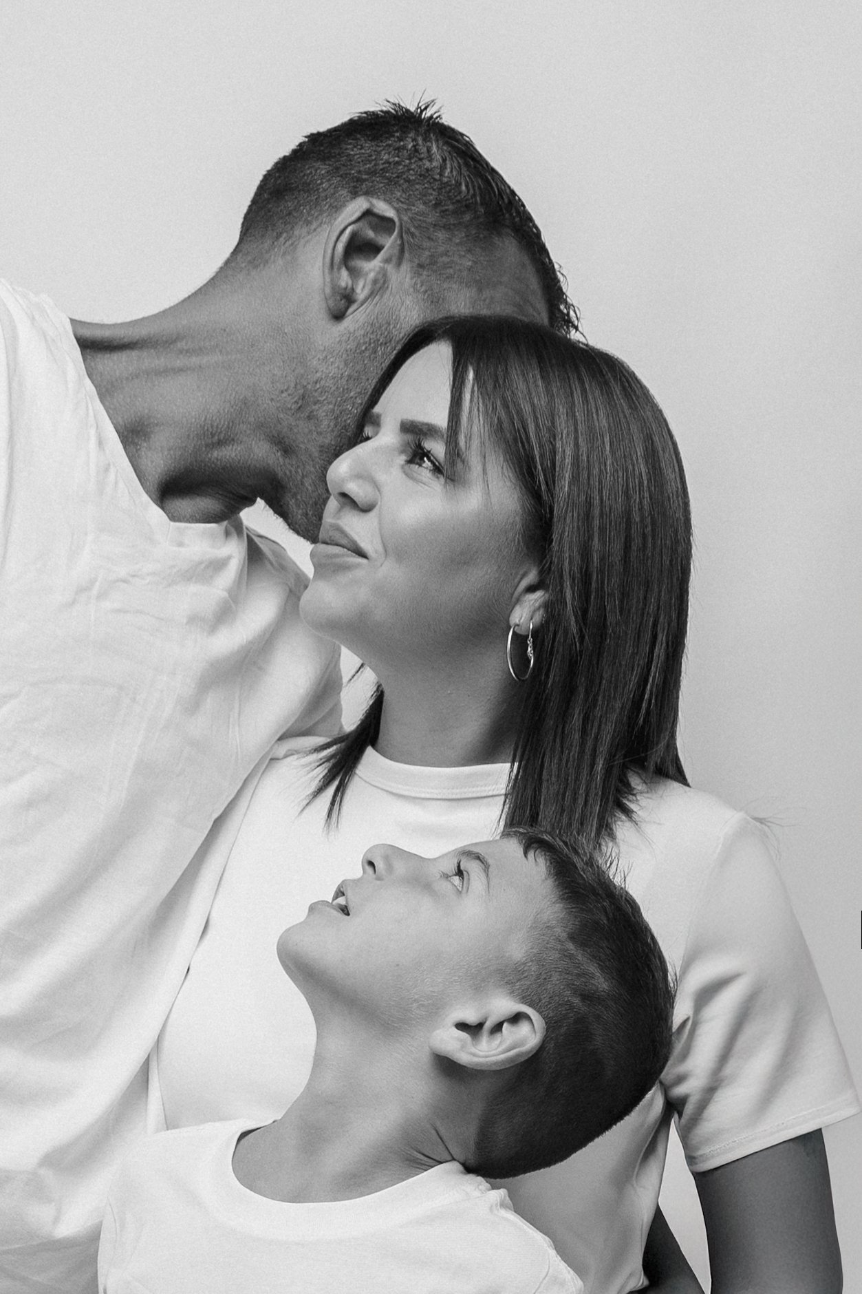 A black and white photo of four people, two adults and two children, looking at each other in close proximity. The man is leaning down to the woman, and the children are looking up at the adults.