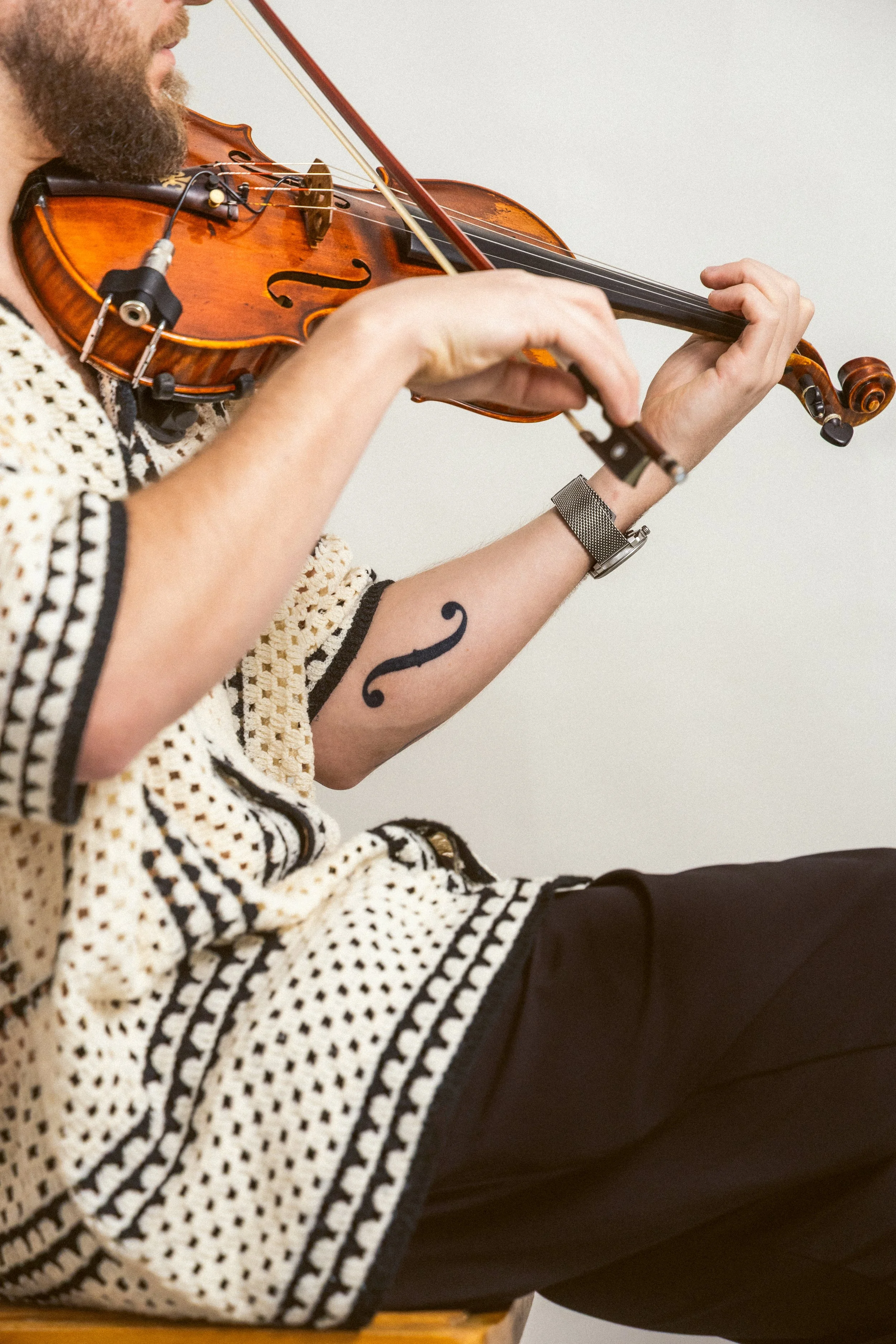 Close-up of a person playing a violin, focusing on their hands, arm, and part of the violin against a light background.