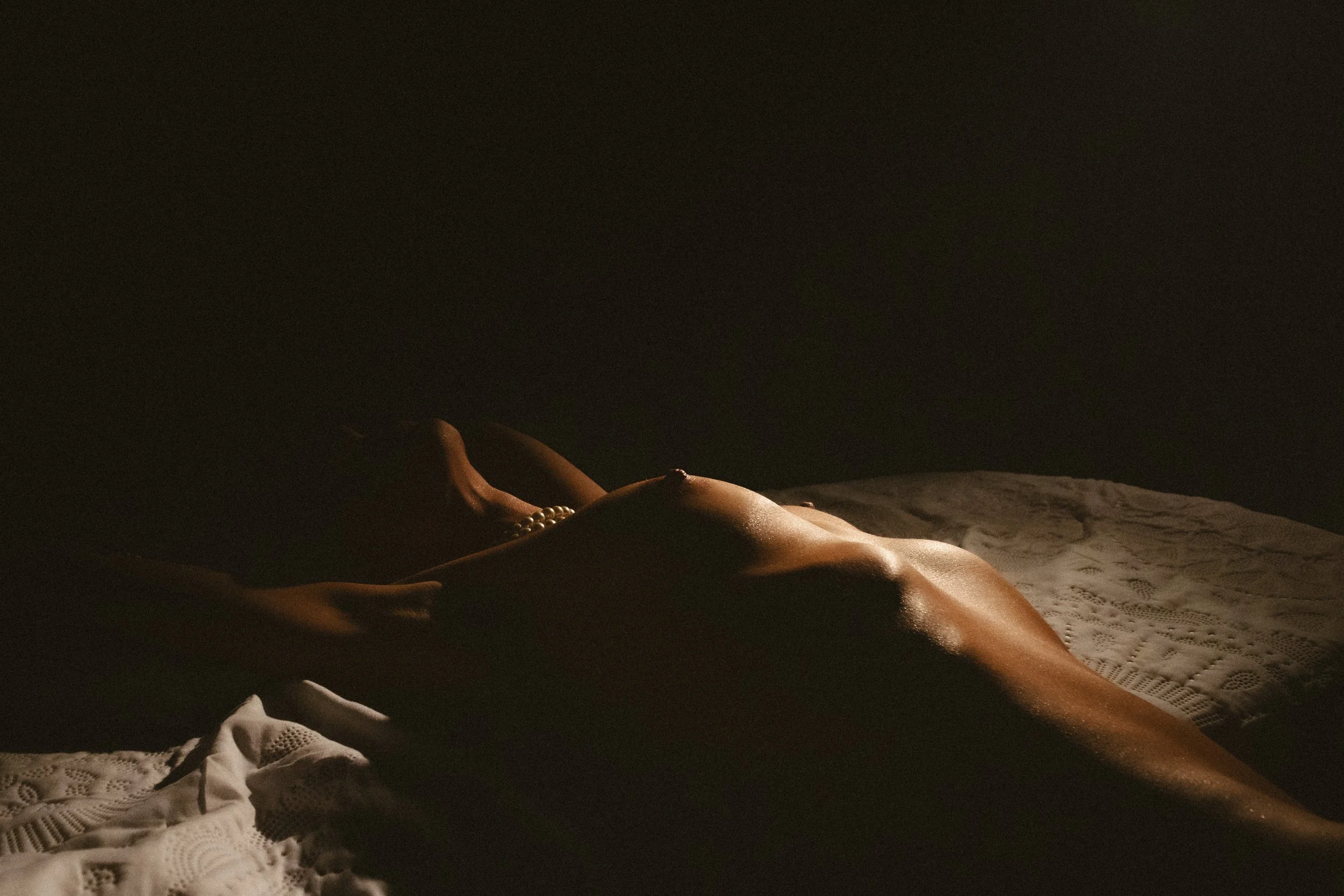 Close-up of a woman's body lying on a bed at night, with soft lighting emphasizing her silhouette, partially covered by a lace nightgown.