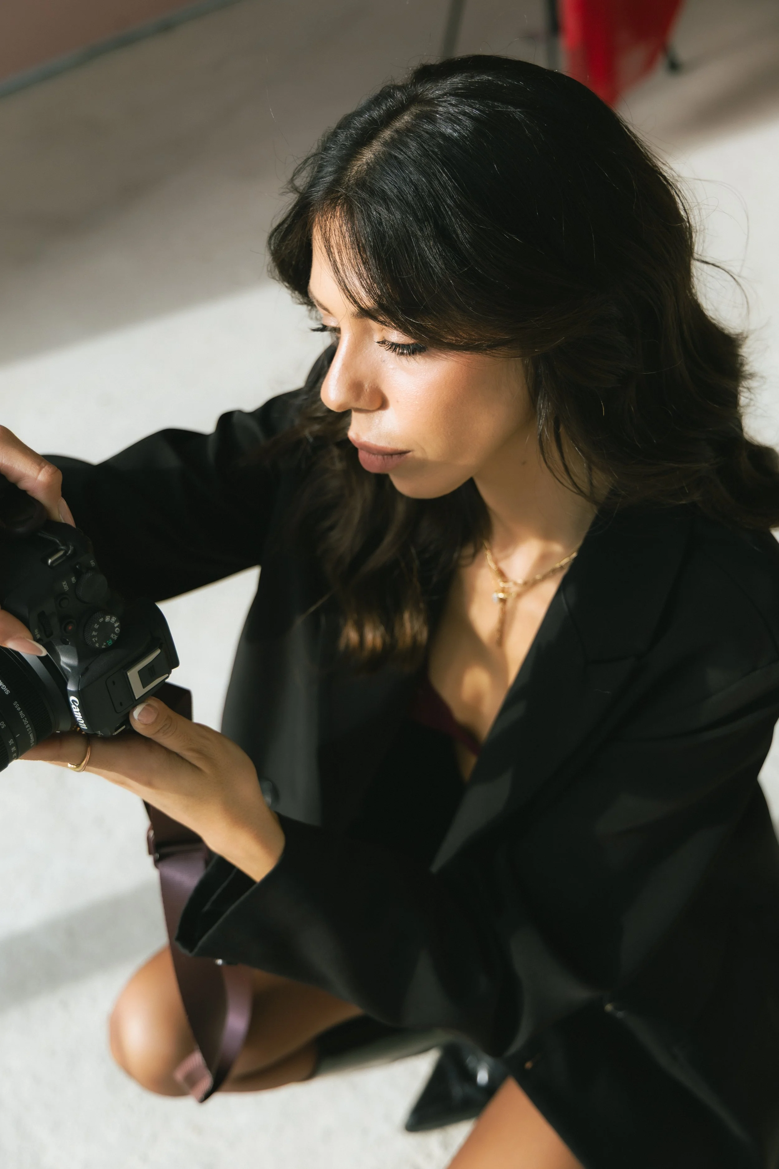 A woman with long dark hair and a black blazer looking at a camera.