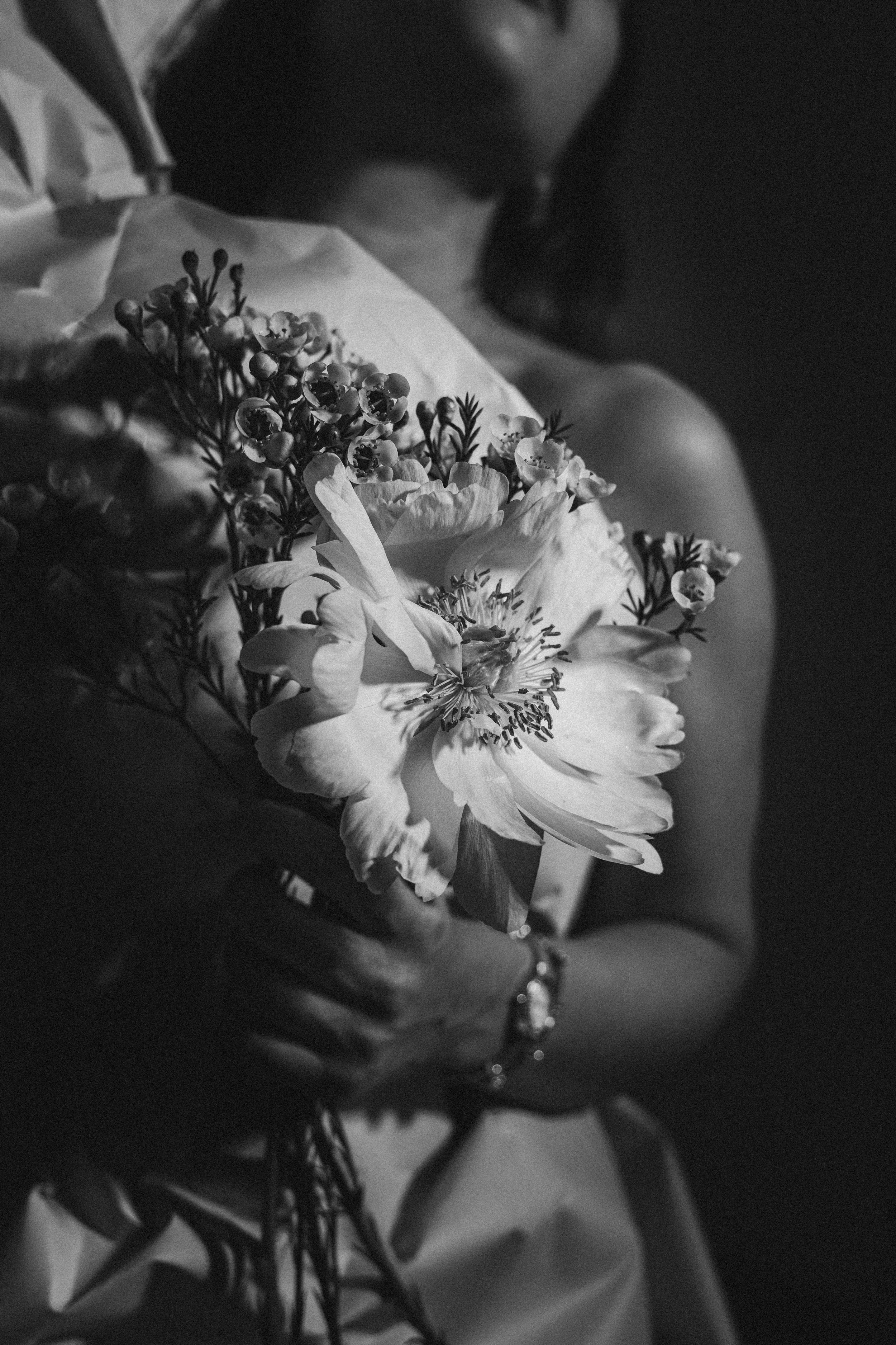 A black and white photo of a person holding a bouquet of flowers, with part of their face and arm visible.