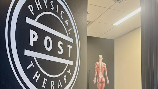 Interior of a physical therapy clinic with a large circular logo on the wall that reads 'Physical Post Therapy' and an anatomical model of a human back in the background.