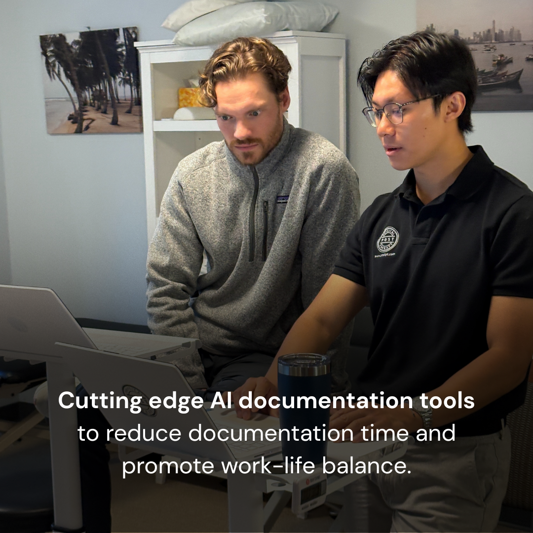 Two men working together looking at a laptop screen in an office space with wall art and a white cabinet in the background. One is wearing a gray fleece jacket, and the other is wearing a black polo shirt with a logo.