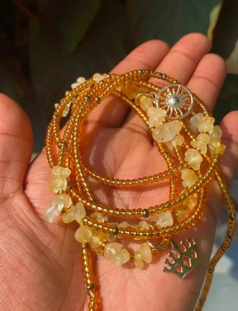 A hand holding multiple gold and beaded necklaces with small white stones and a crown-shaped pendant.
