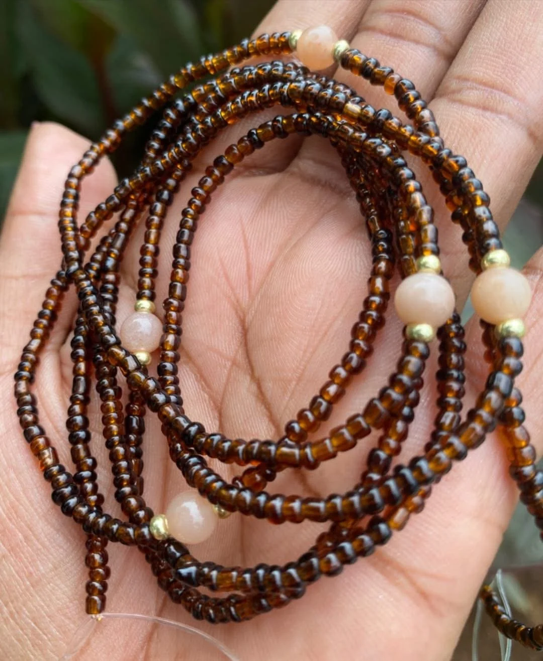 A hand holding a string of brown beaded necklaces with pearl and gold-colored bead accents.