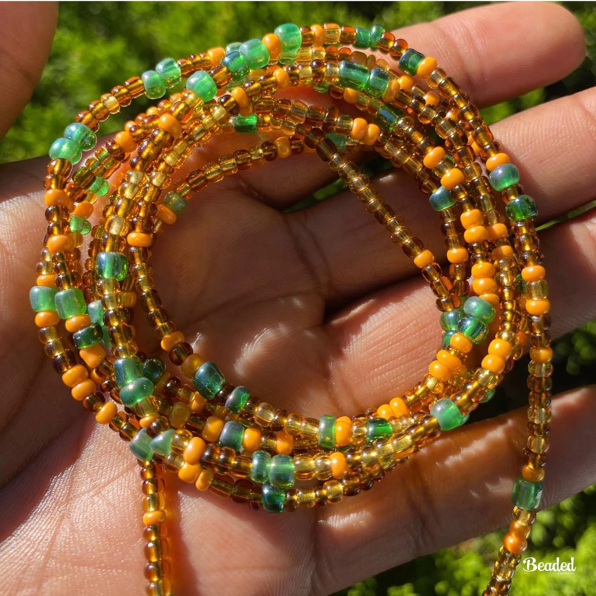 Close-up of colorful beaded jewelry with green, yellow, and amber beads, held in a person's hand outdoors.