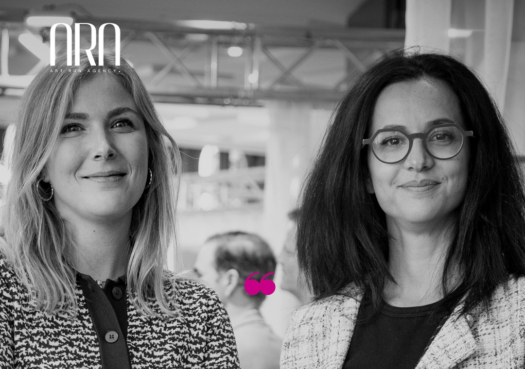 Dos mujeres sonriendo en un ambiente de interior, en un evento o reunión, en fotografía en blanco y negro.
