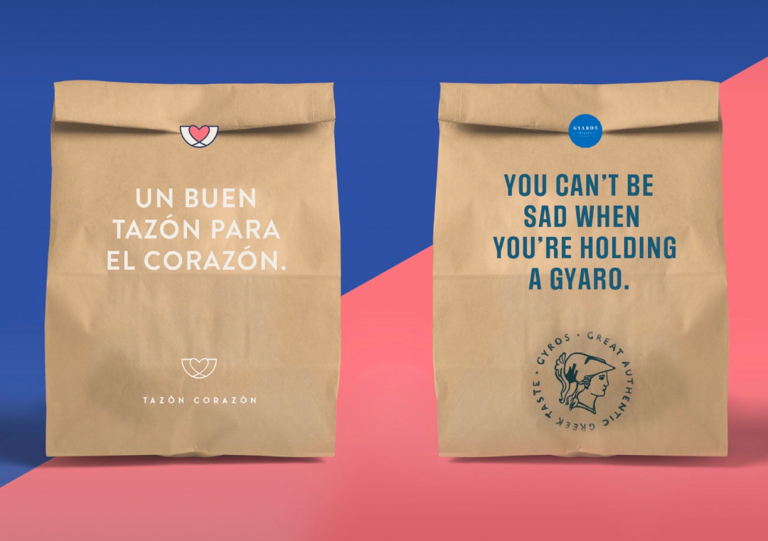 Dos bolsas de papel con mensajes en español e inglés, una con un corazón y la otra con un dibujo de un gaviotón. Fondo rosa y azul.