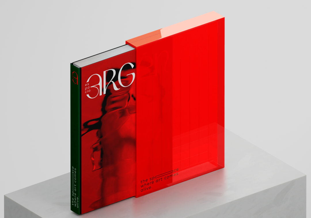 Libro de arte con cubierta roja y diseño abstracto, parcialmente cubierto por una caja transparente de color rojo, en una superficie blanca.
