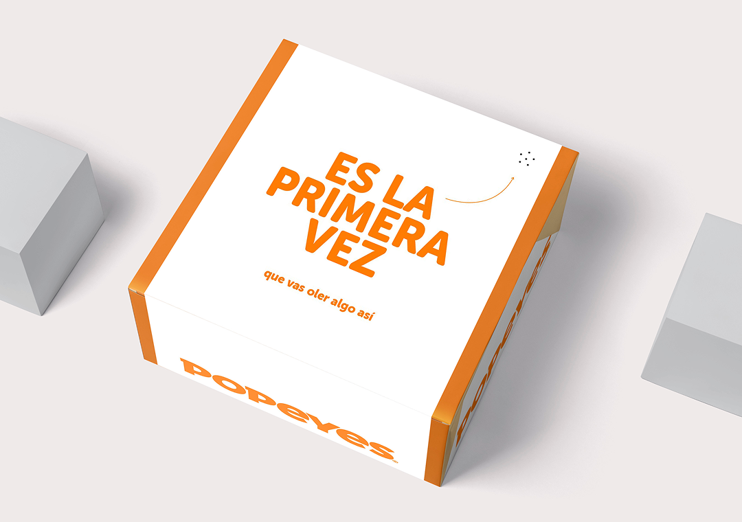 Caja decorativa con letras en color naranja que dice 'Es la primera vez que vas oler algo así' y la palabra 'Popeyes' en la parte inferior