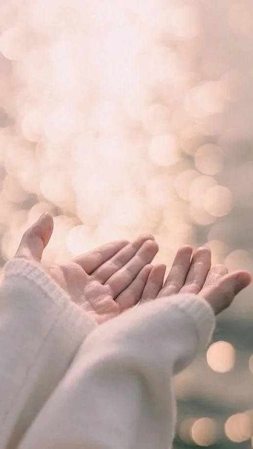 Mains d'une personne en pull léger, tendues vers le ciel avec un fond flou de lumières chaudes et bokeh.