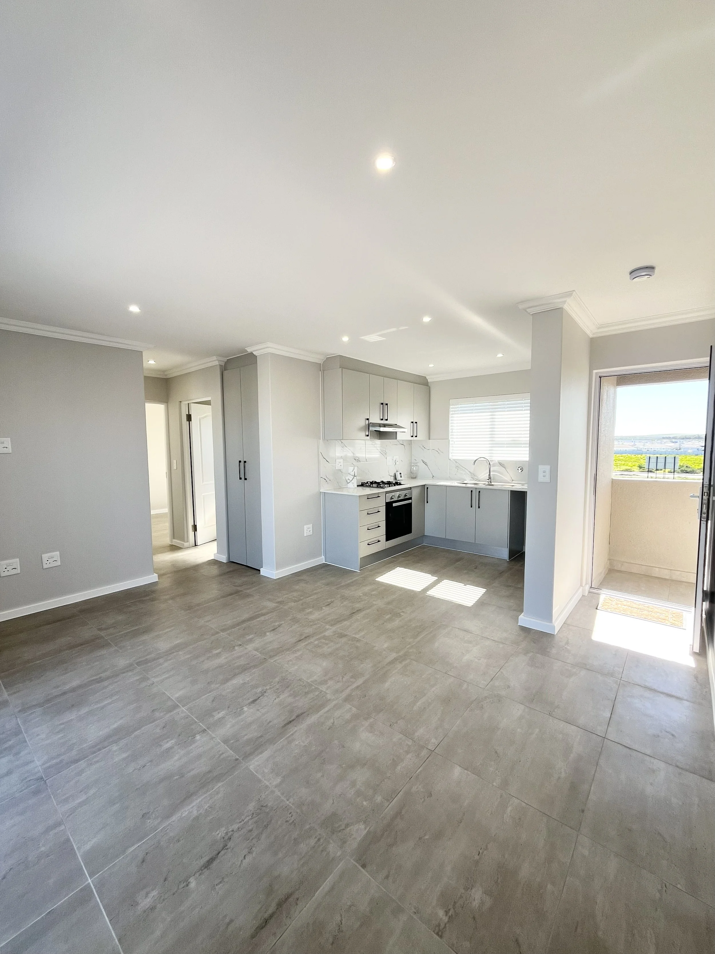 Modern kitchen with gray cabinets, marble backsplash, stainless steel appliances, and large gray floor tiles, with a sliding door leading to a balcony.