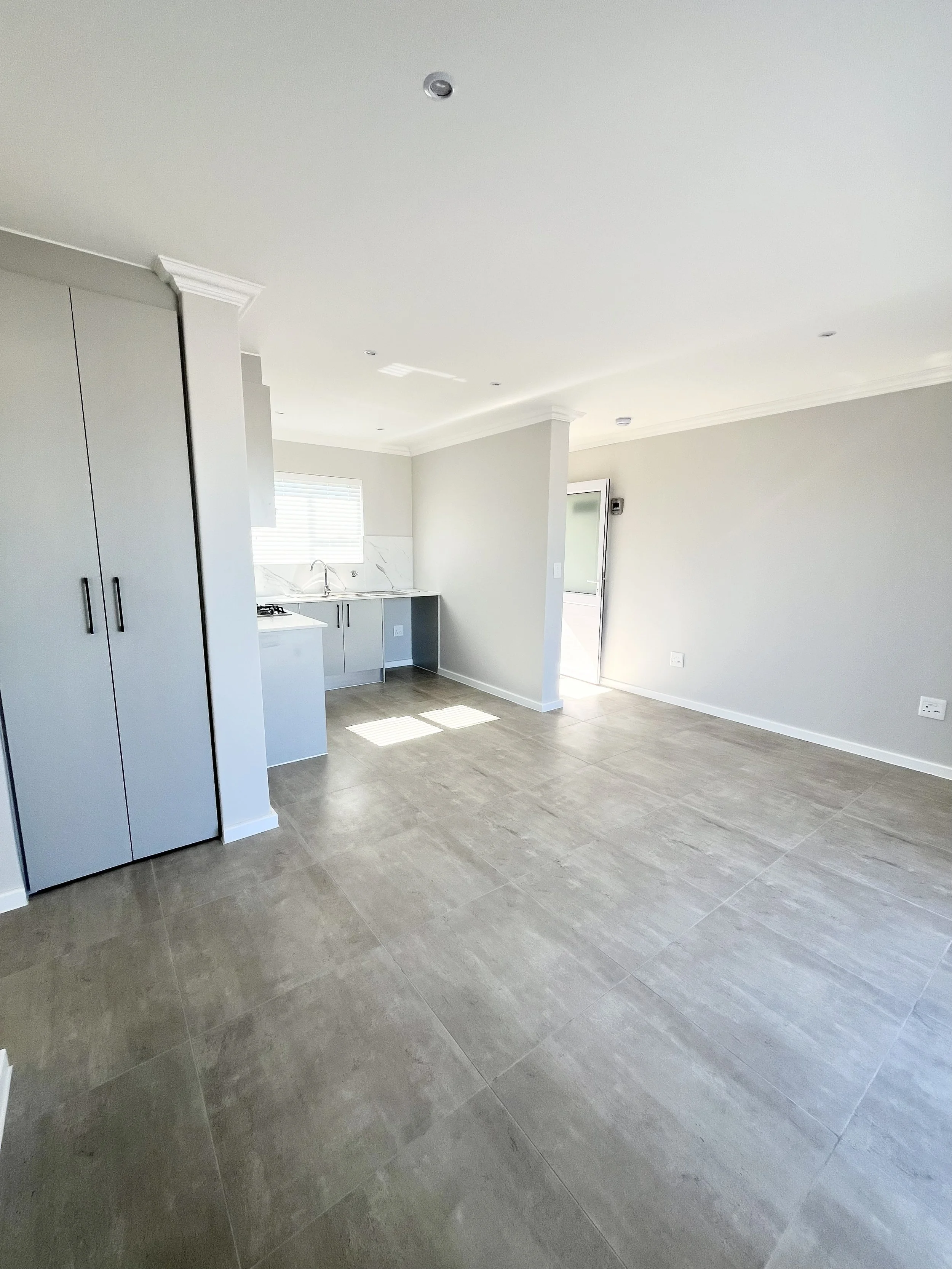 Empty modern kitchen with grey cabinets, white countertops, tile flooring, a window, and a door to outside.