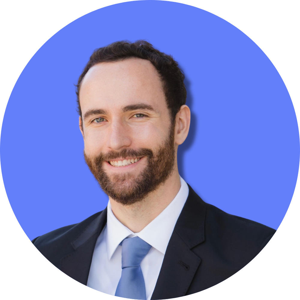 A smiling man with a beard in a suit and tie against a blue background.