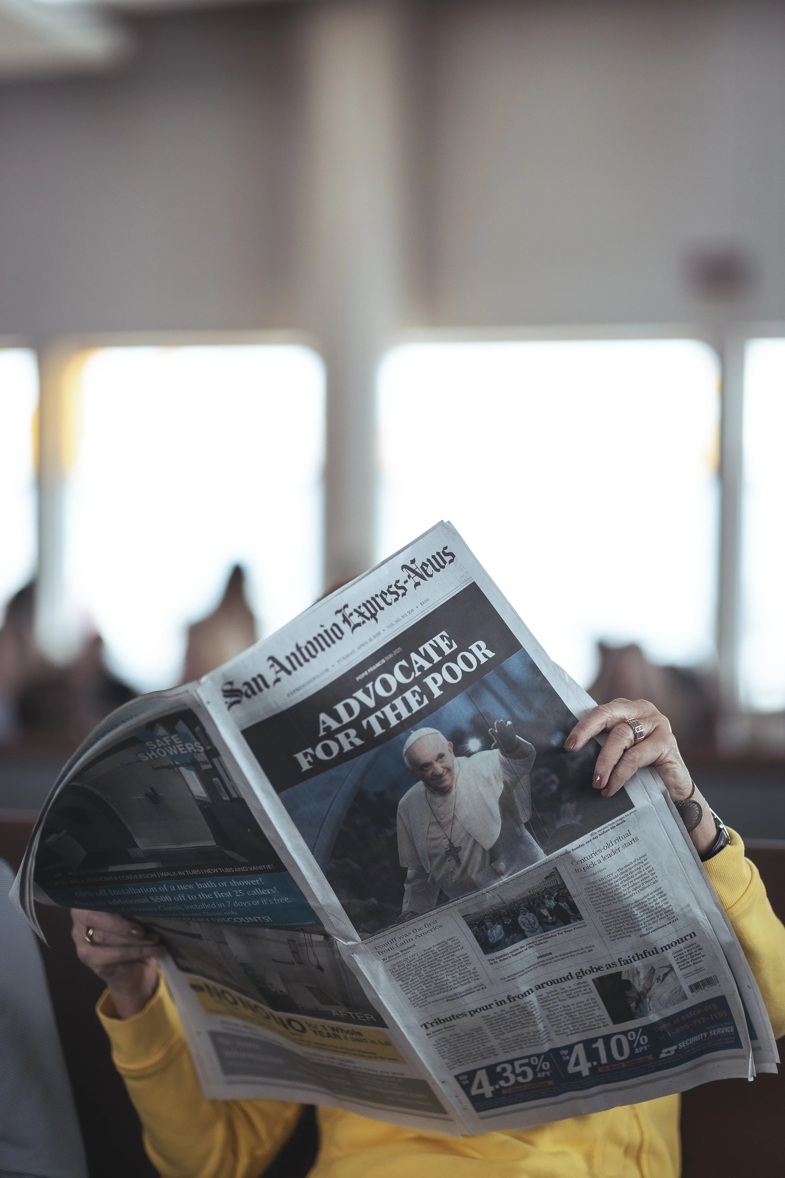 Person reading the front page of a newspaper titled 'San Antonio Express-News' with a photo of Pope Francis on the cover.