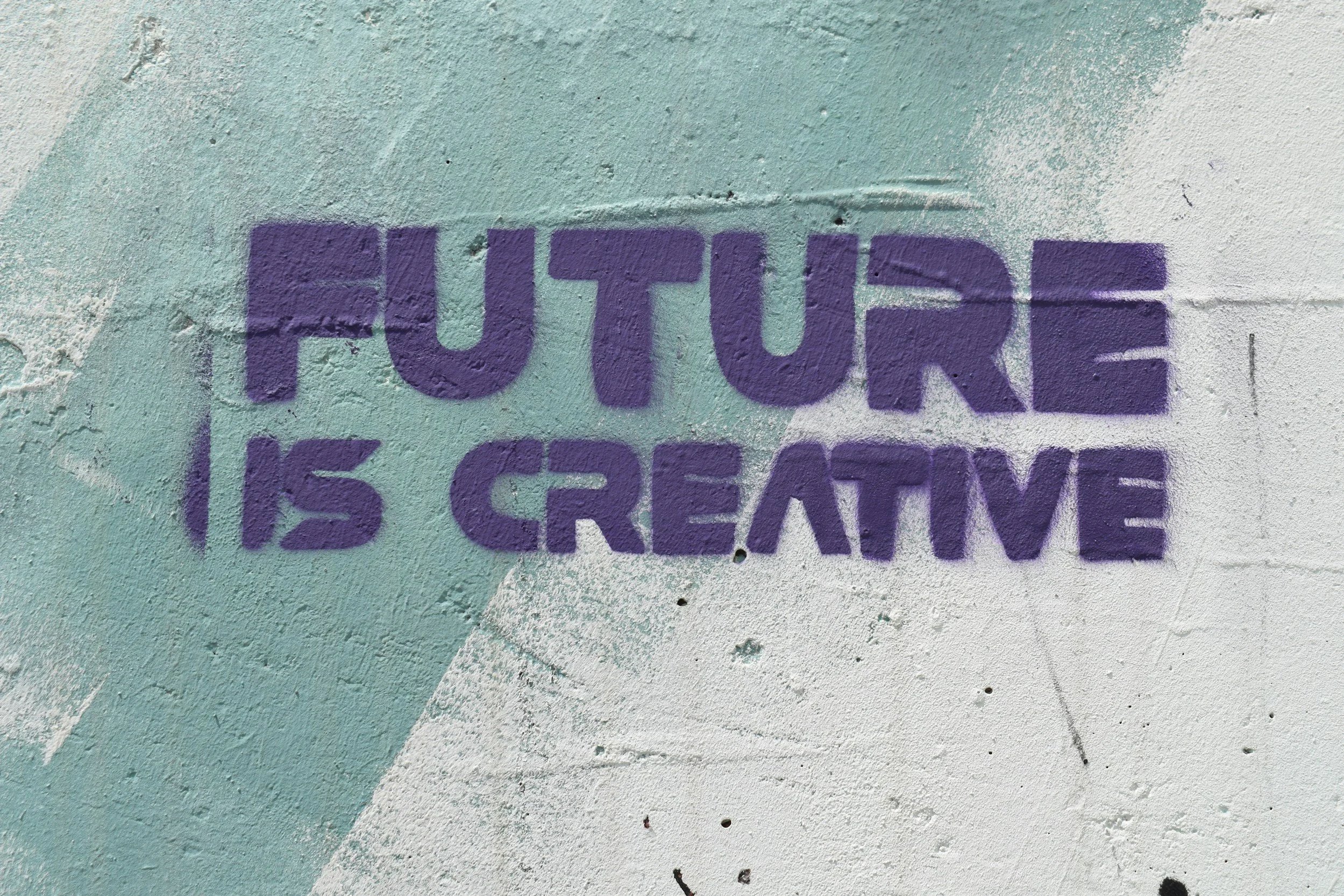 Graffiti on a wall with the words "FUTURE IS CREATIVE" spray painted in purple letters.