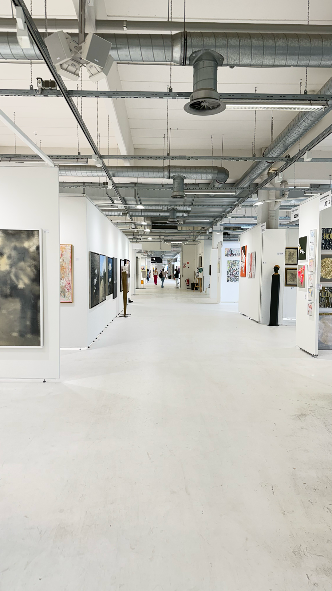 An art gallery with white walls displaying various paintings and sculptures, with a view down a long corridor of artwork and visitors.
