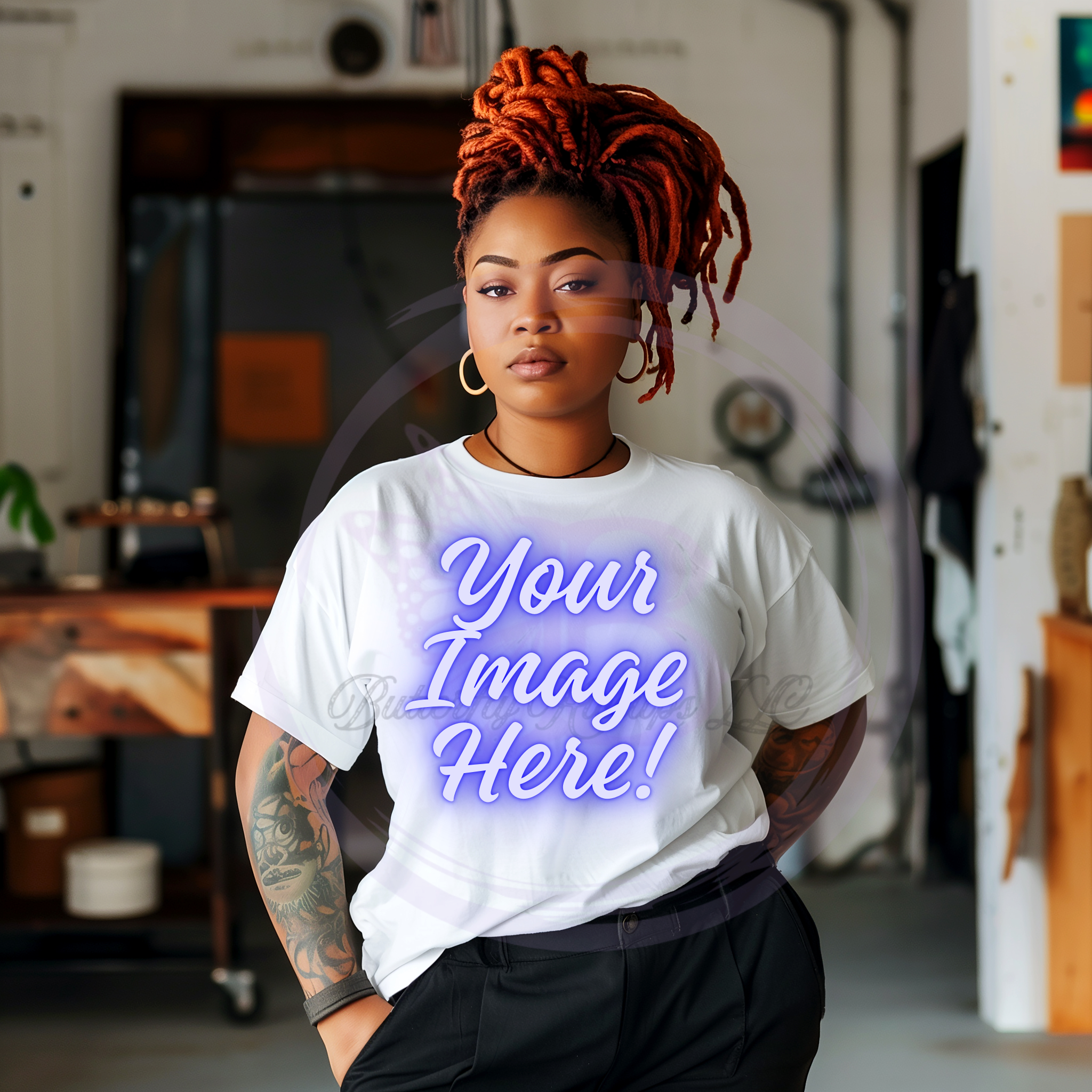 A woman with orange dreadlocks, wearing a white t-shirt with purple text and black pants, standing in an interior space with bookshelves and artwork in the background.