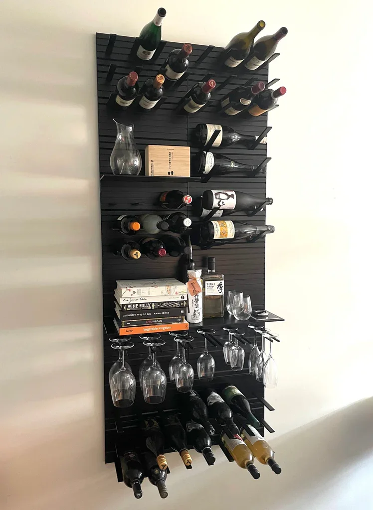 Wall-mounted wine rack holding multiple bottles of wine, wine glasses hanging upside down, a glass pitcher, books, a bottle of Toki whiskey, and wine accessories.